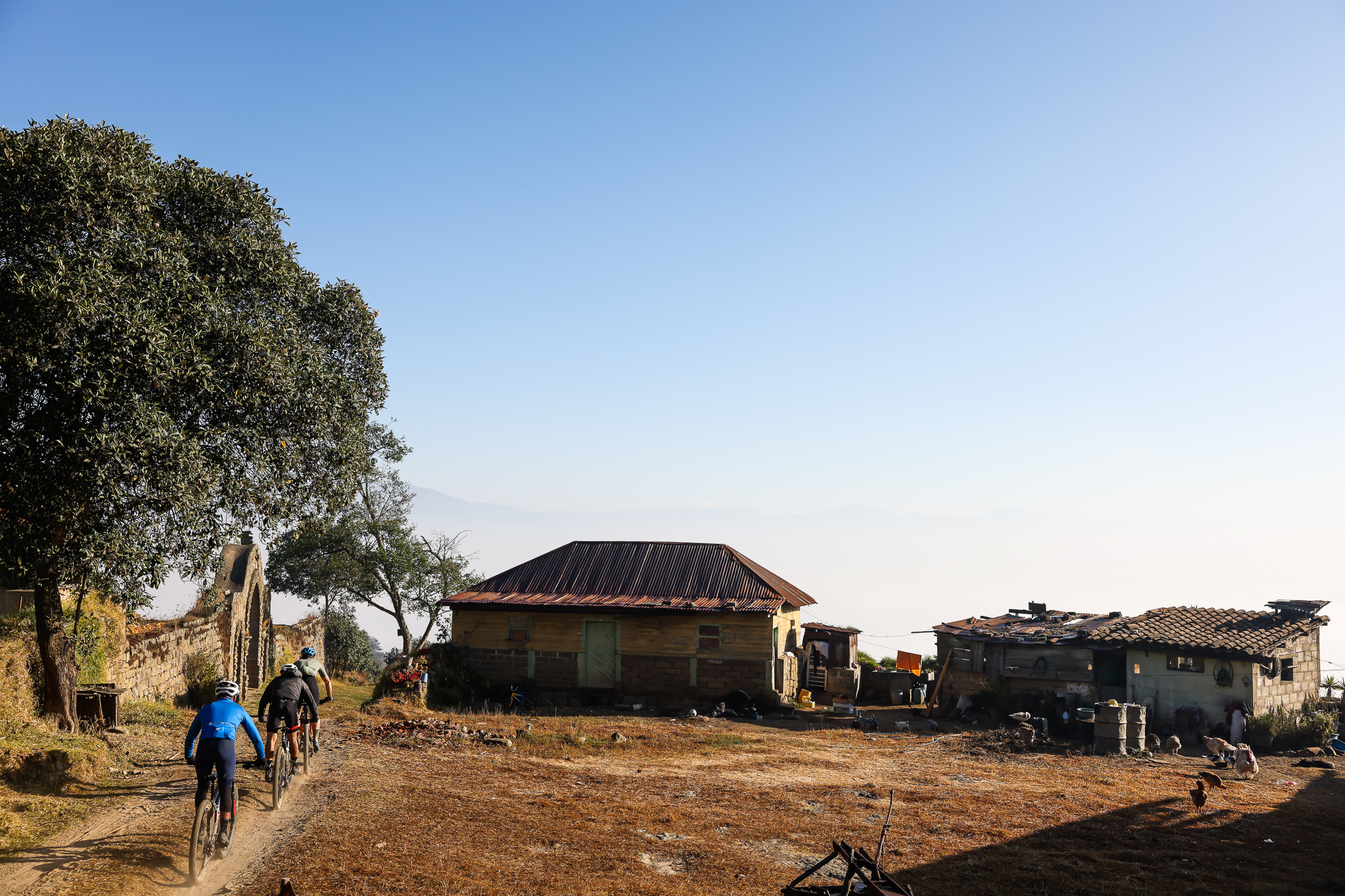 Three riders climbing a dirt track past tin-roofed houses on a ridge