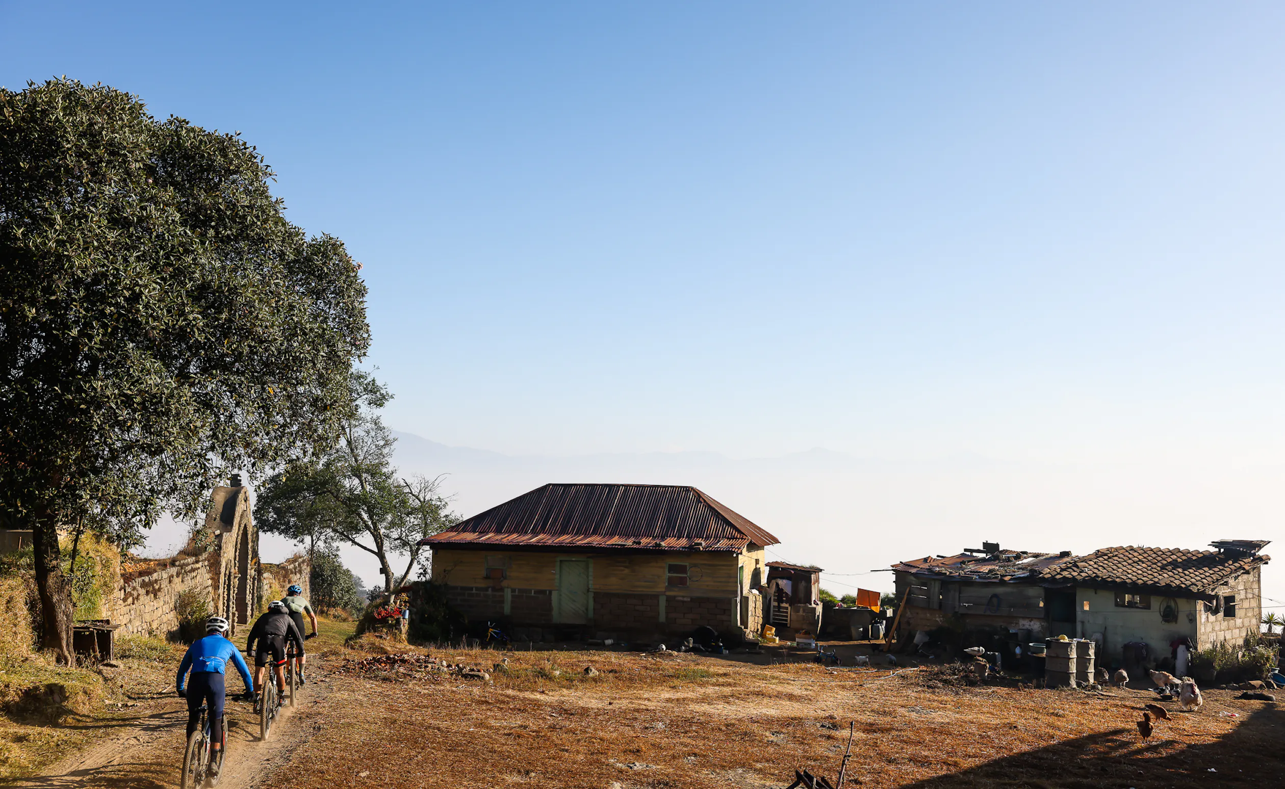 Three riders climbing a dirt track past tin-roofed houses on a ridge