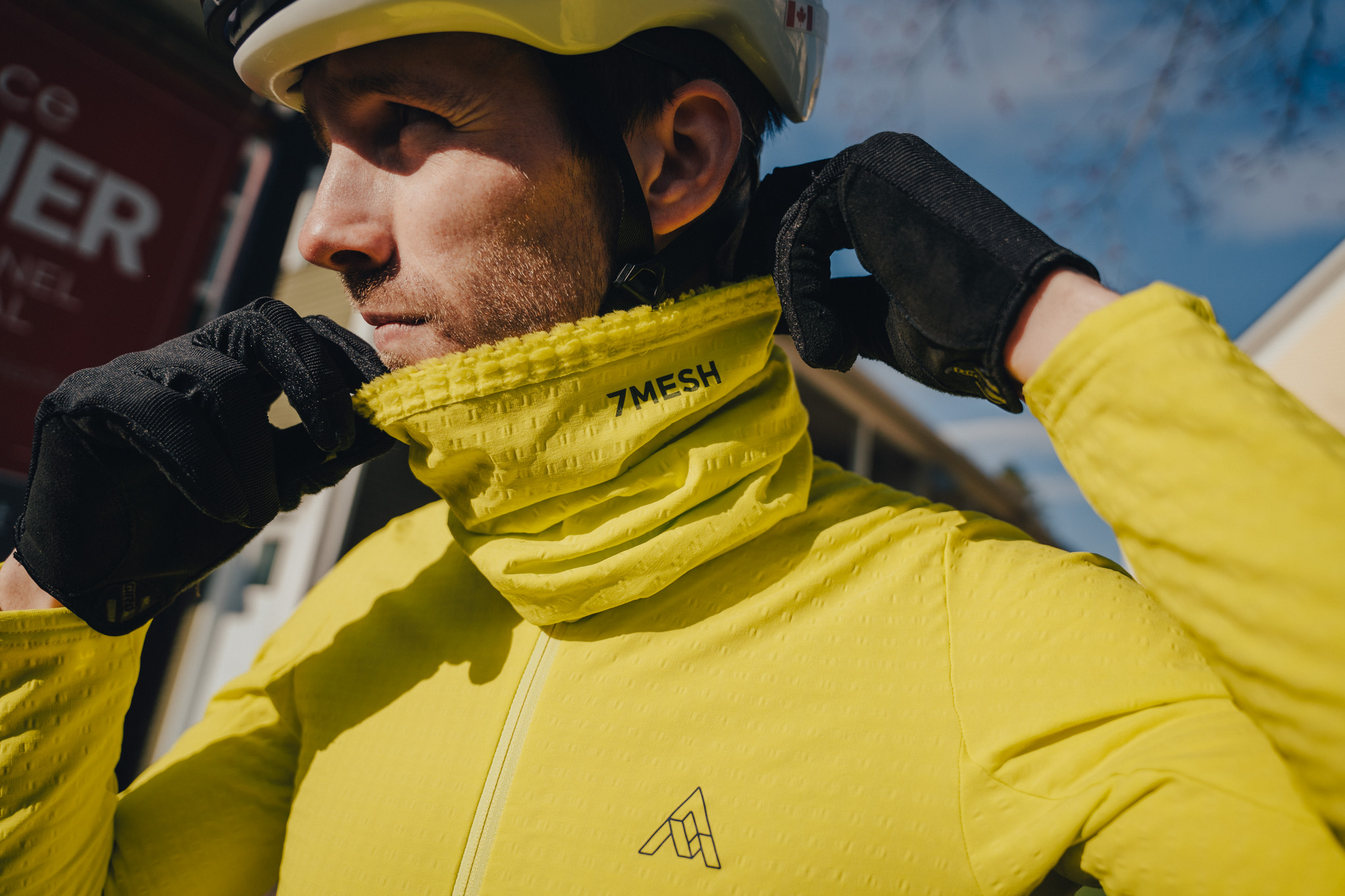 Rider pulling a yellow 7mesh neck warmer up over the chin in winter sunlight