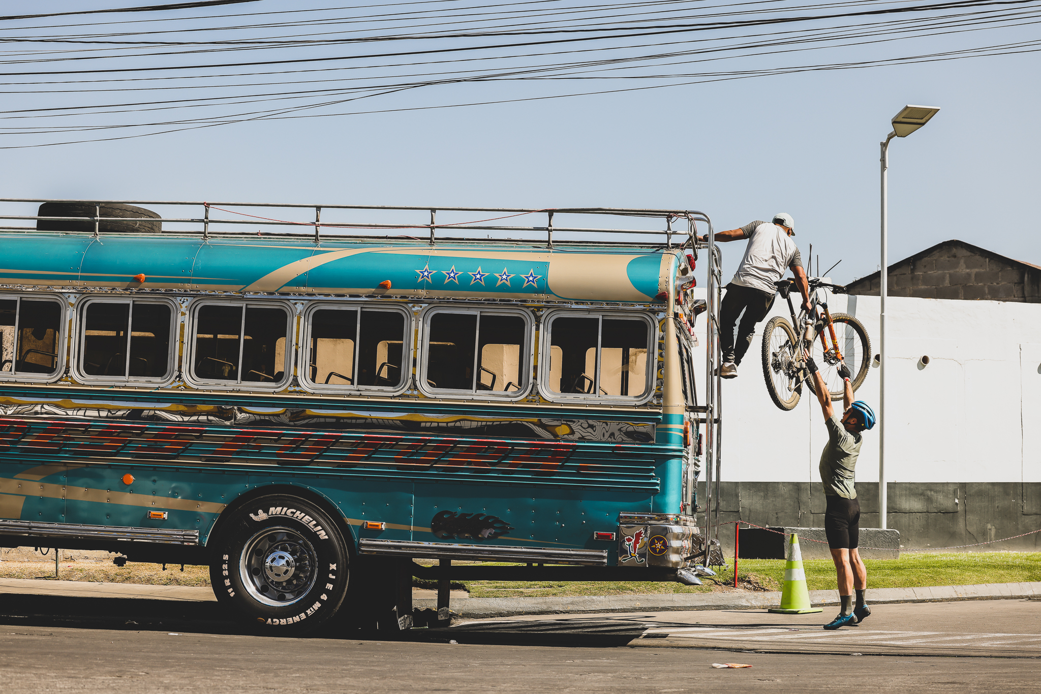 A mountain bike being lifted onto the roof rack of a painted chicken bus