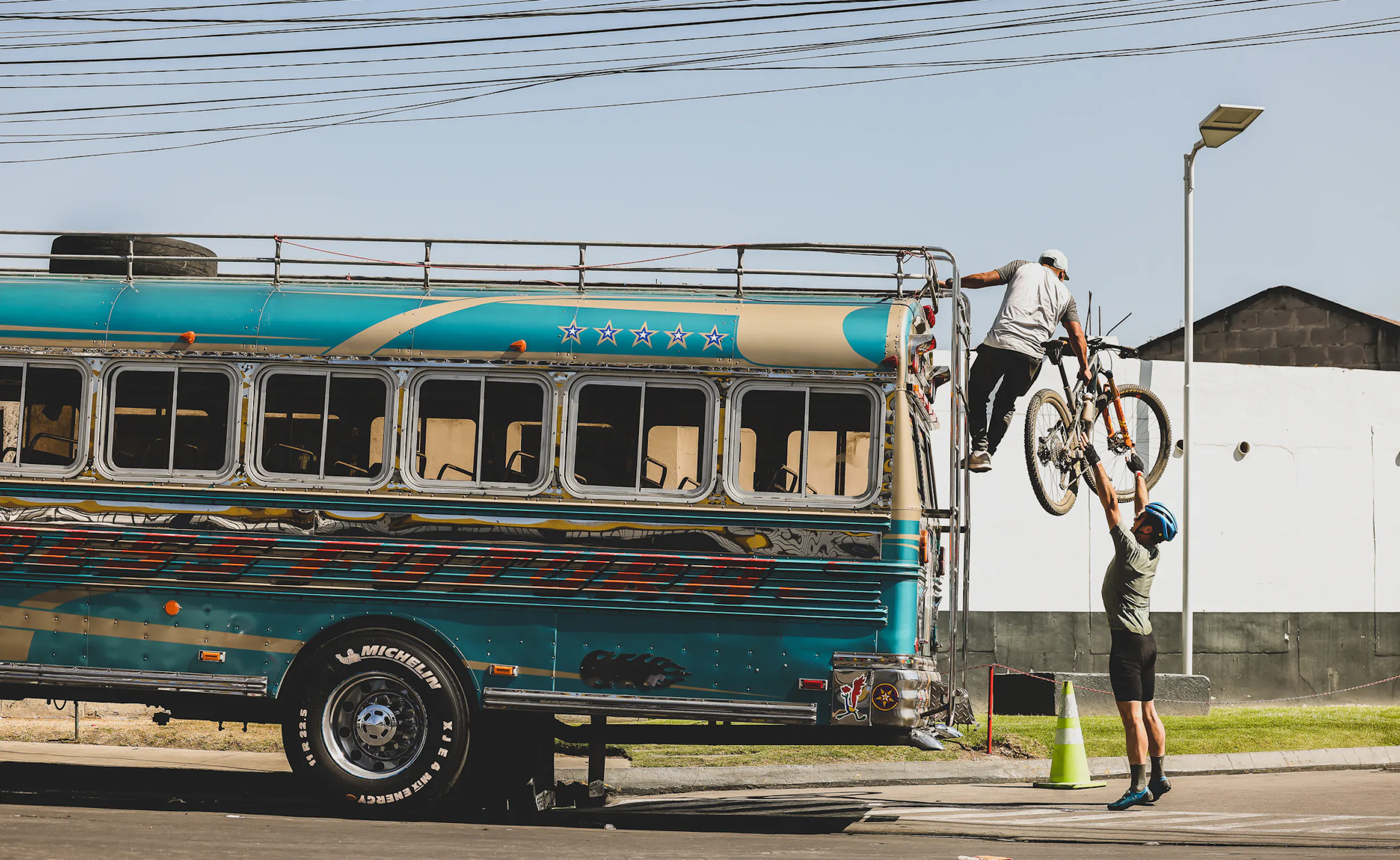 A mountain bike being lifted onto the roof rack of a painted chicken bus