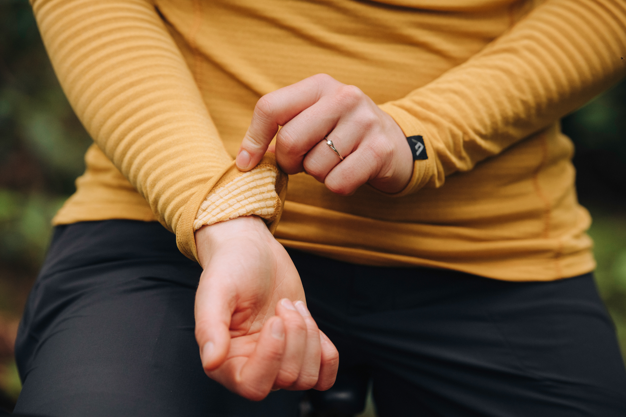 Close-up of hands pulling back a mustard merino base layer sleeve at the wrist