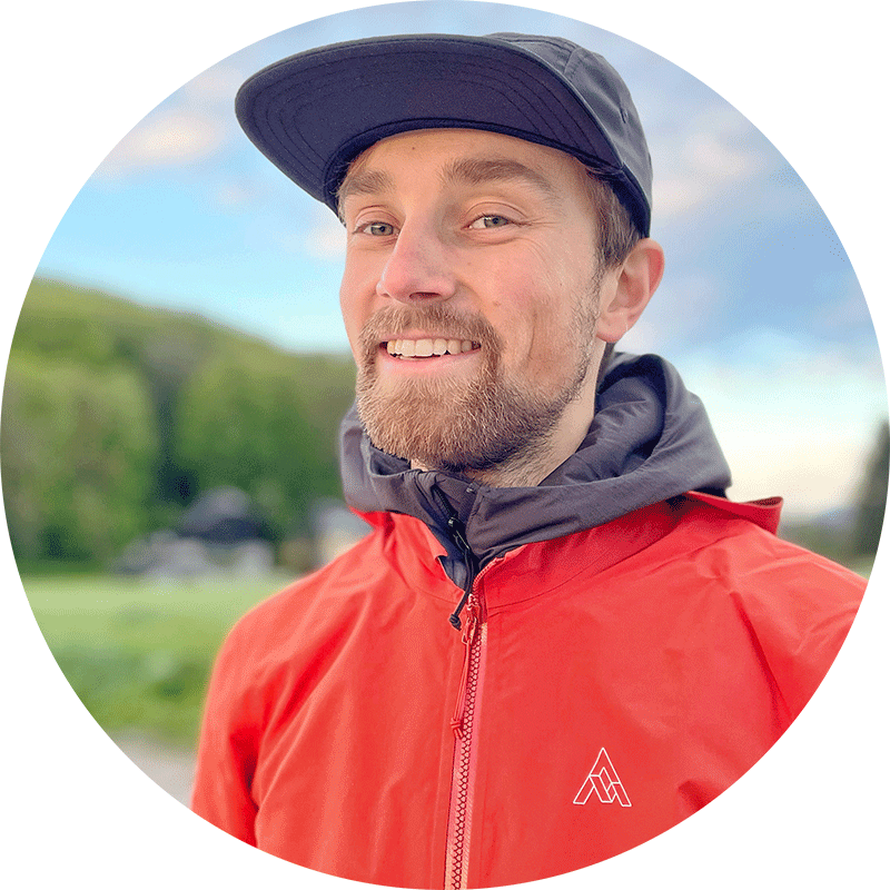 Max Riese in a cap and red hooded jacket, green hills behind him