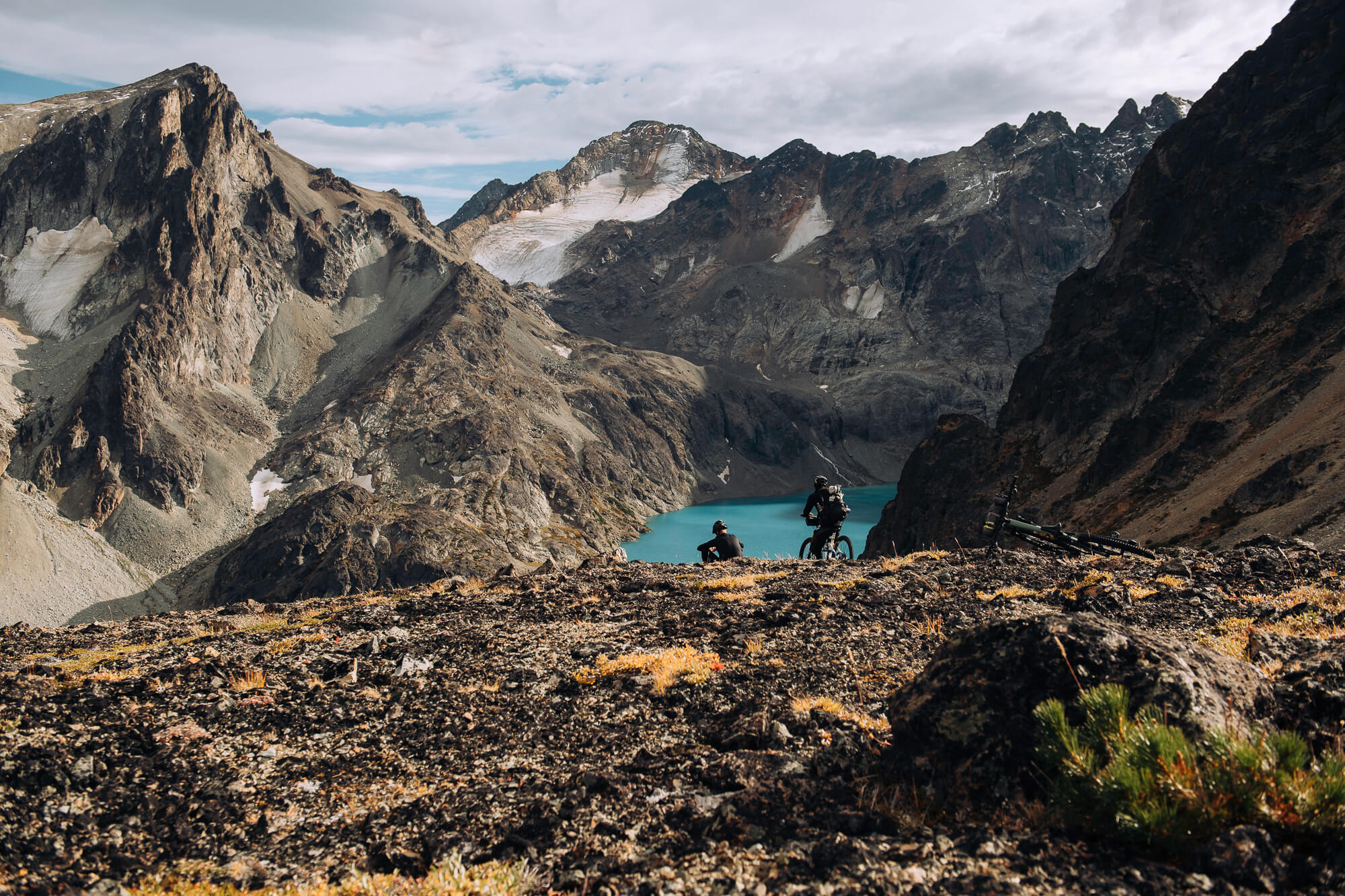 Two riders resting on a rocky outcrop above a turquoise lake