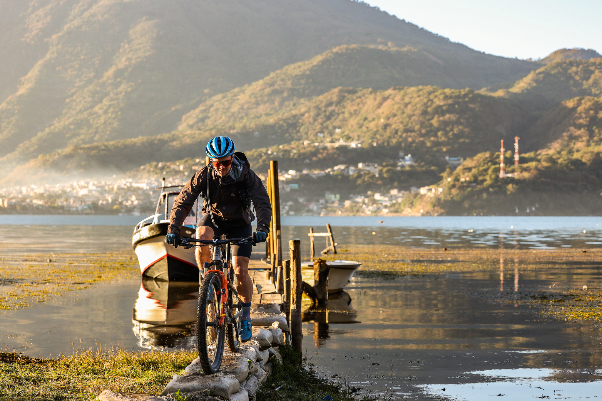 Rider riding off a wooden jetty onto the shore of a lake below green hills