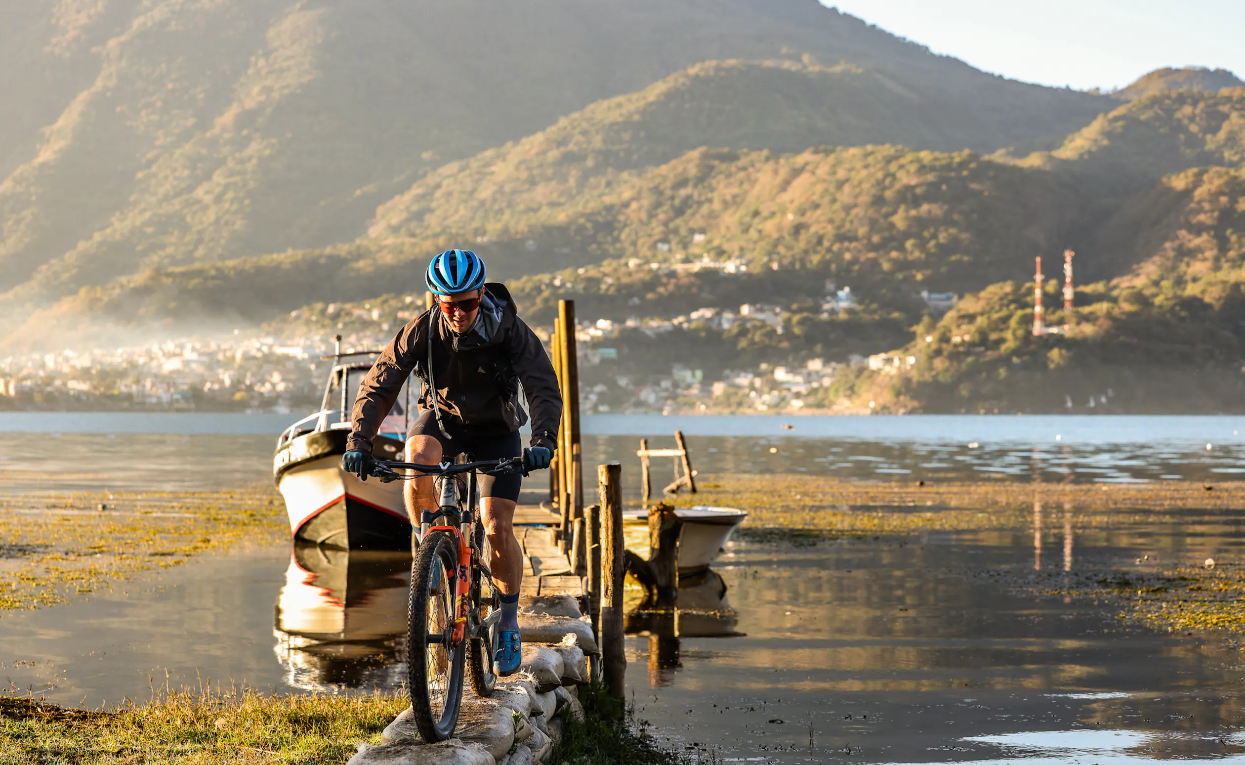 Rider riding off a wooden jetty onto the shore of a lake below green hills