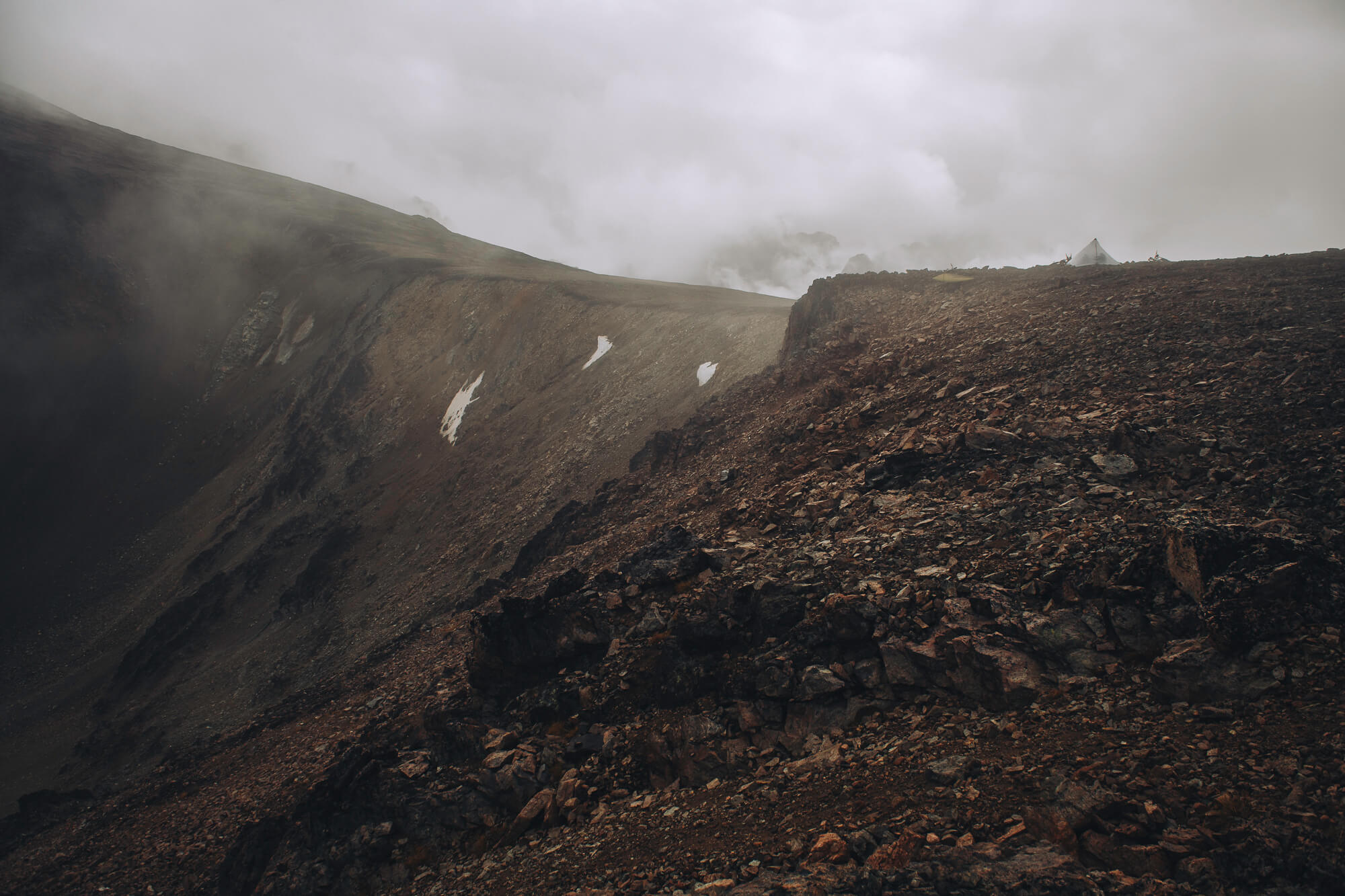 A single tent pitched on a rocky ridge in blowing cloud