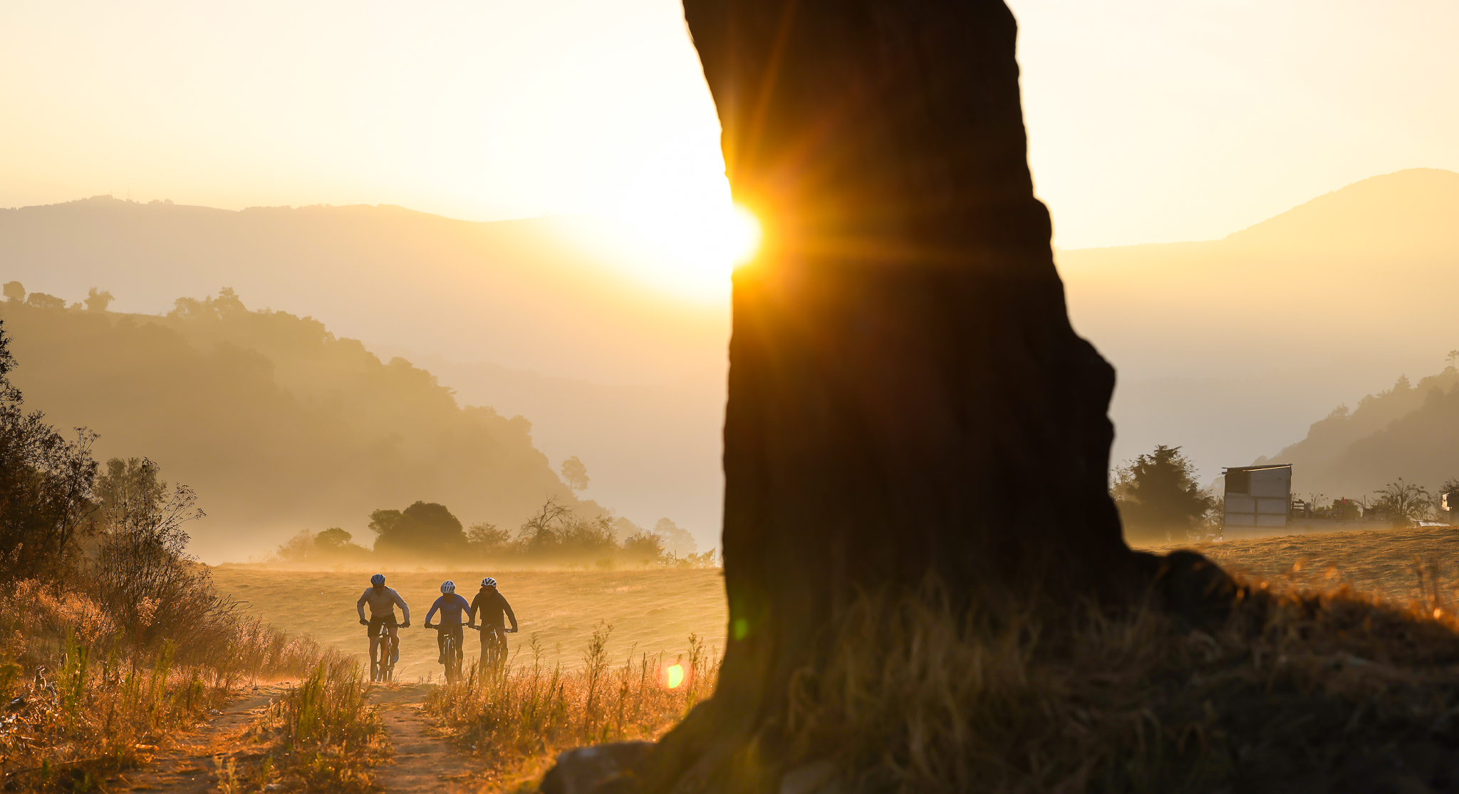 Three riders silhouetted on a dusty track riding into low sun
