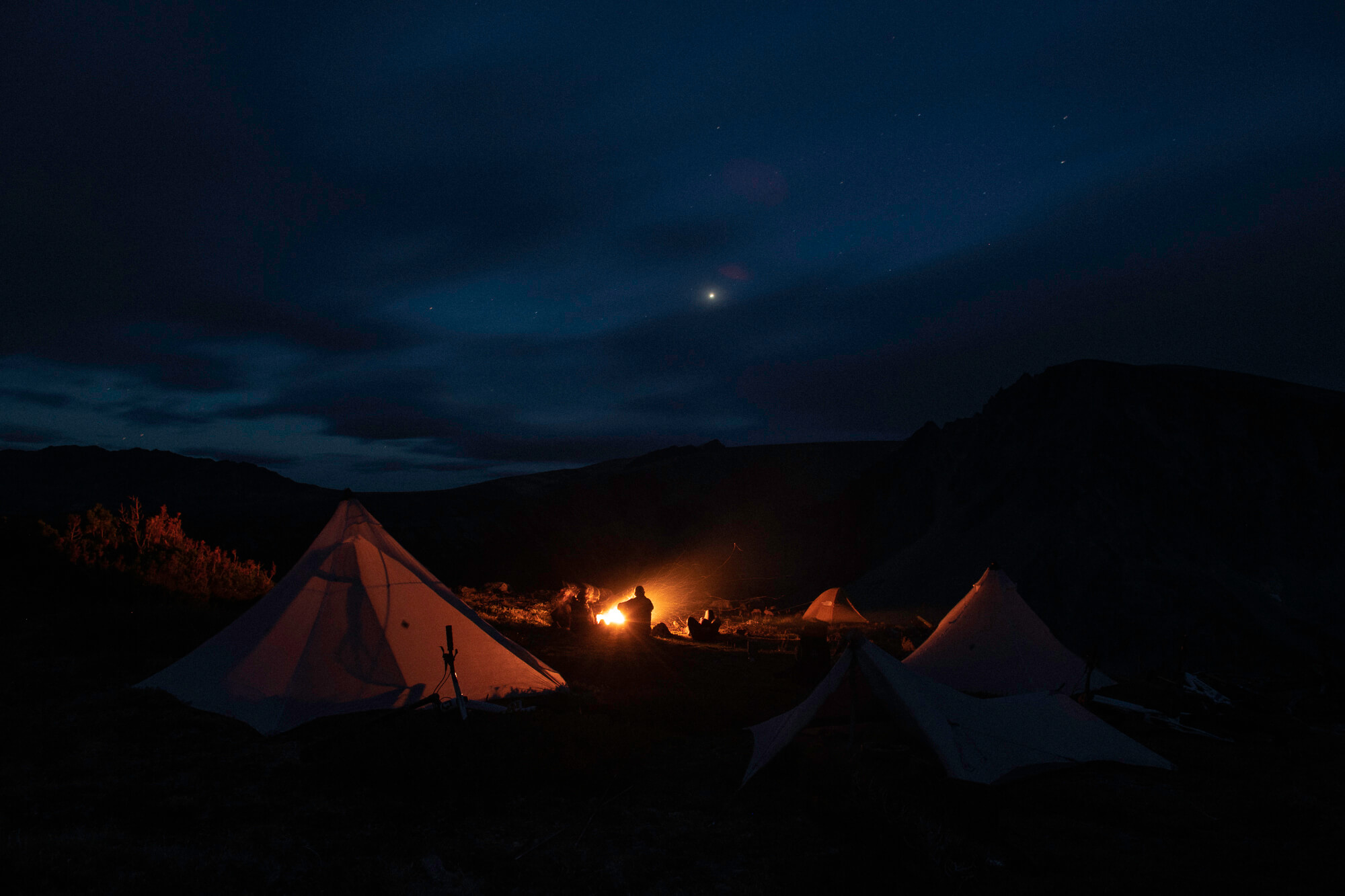 Three pyramid tents around a campfire under a night sky