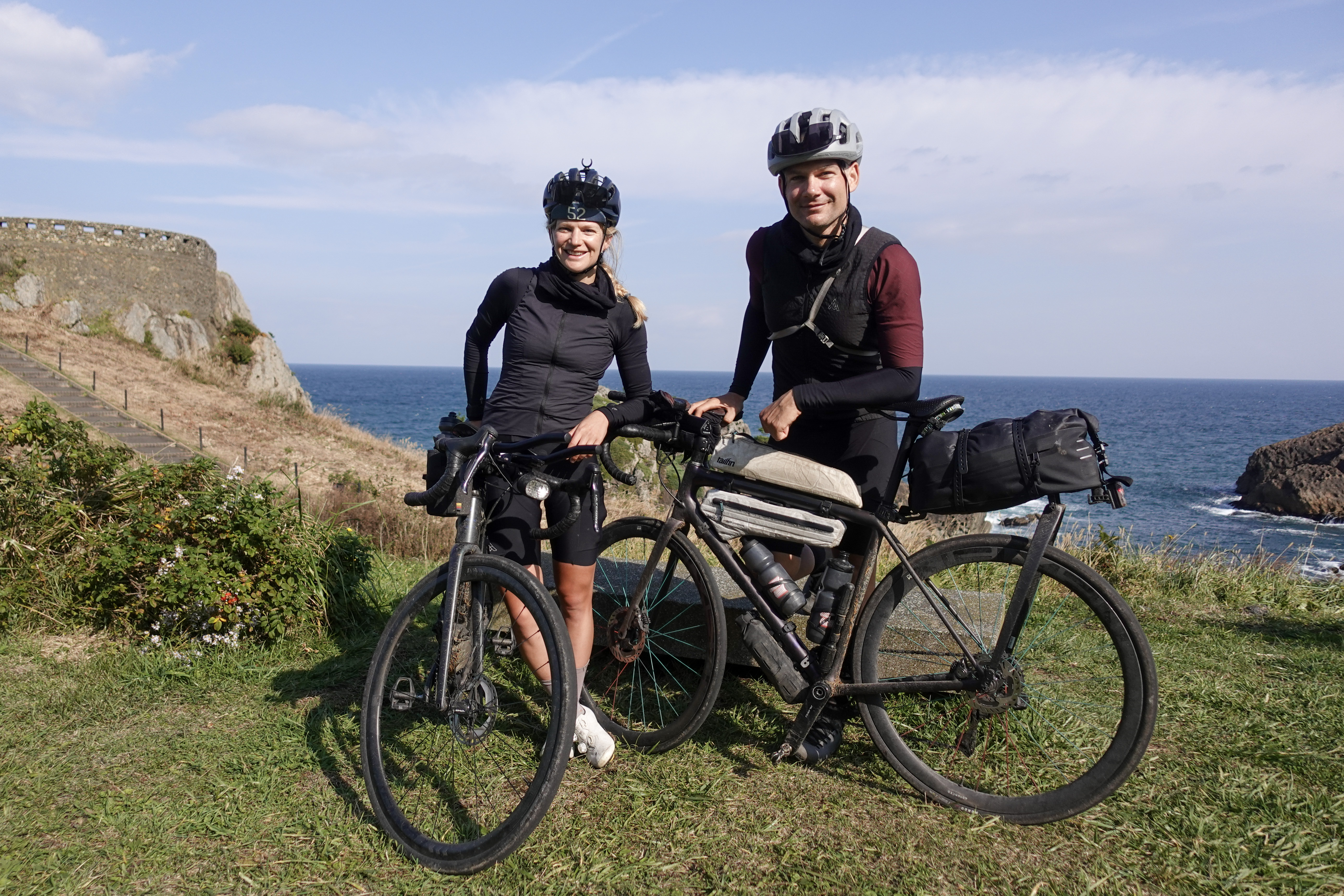 Alexander Kopp and Jana Kesenheimer with loaded bikes on a grassy headland above the sea