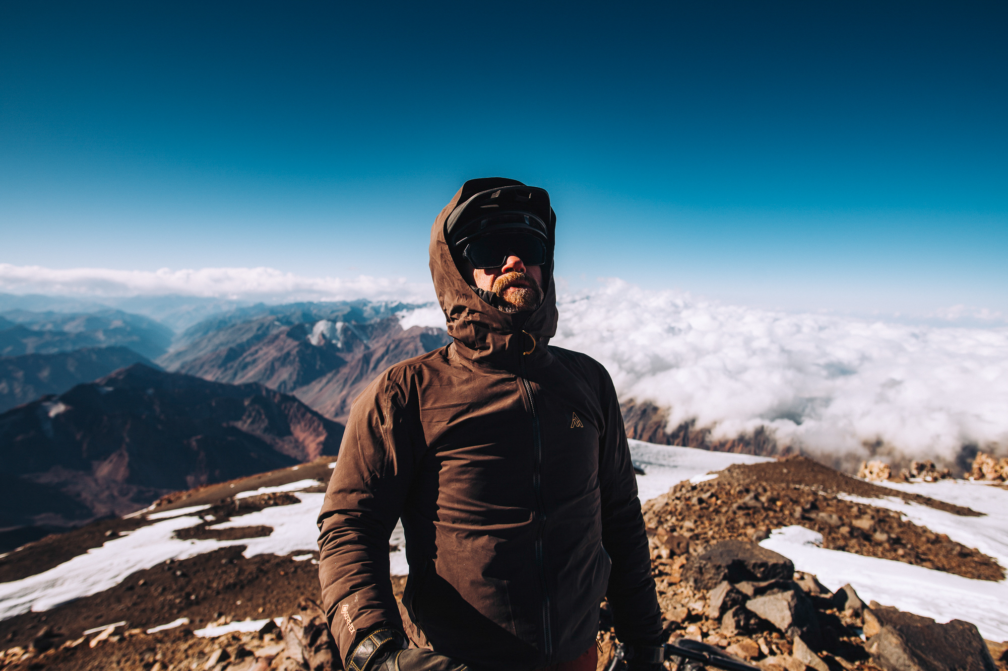 Portrait of a rider hooded and goggled on a snowy summit above cloud