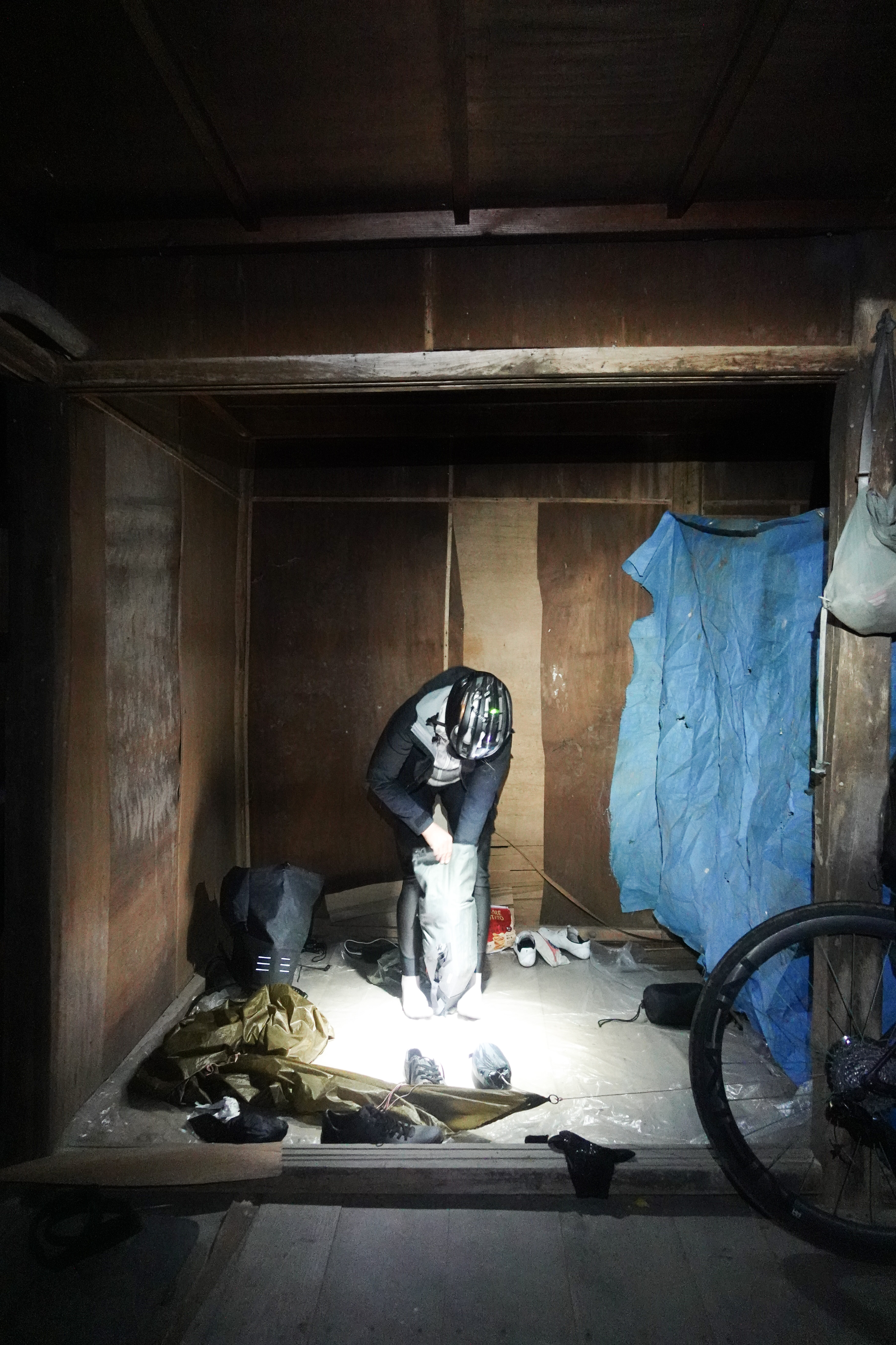 Rider packing a sleeping bag in a bare wooden shelter lit by one lamp