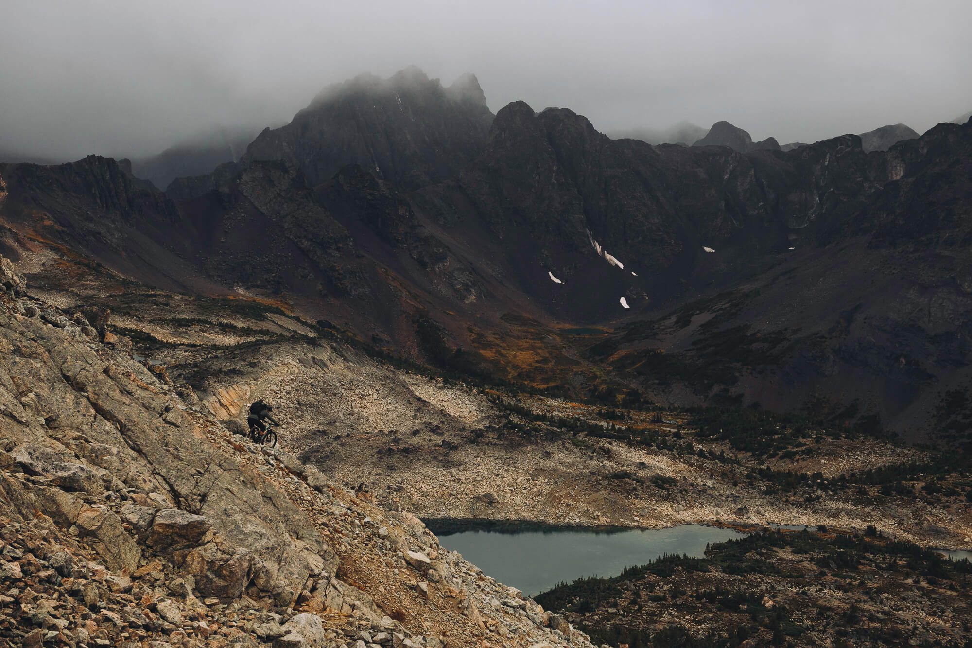 Rider descending a steep rocky slope high above a valley lake