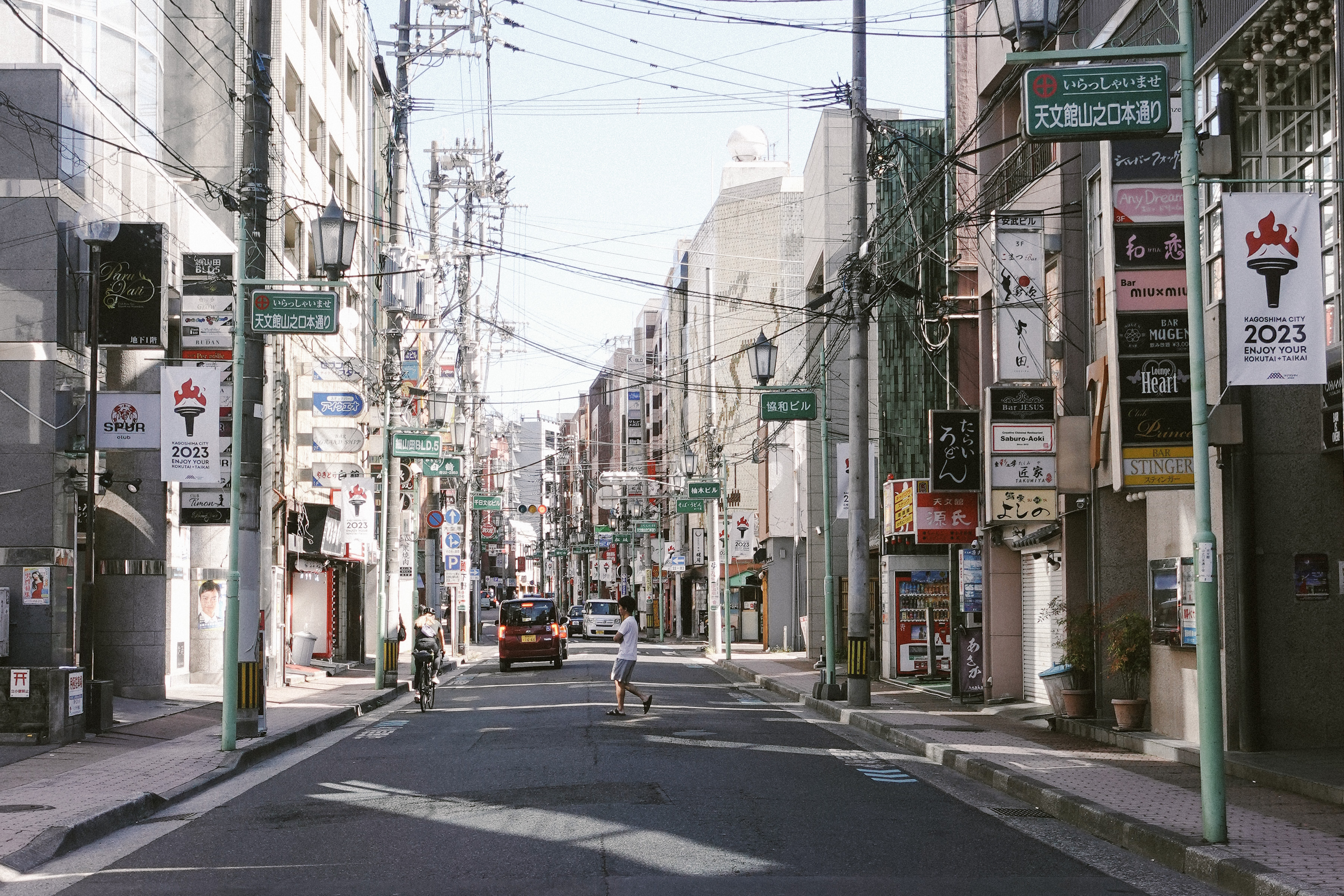 Cyclist and pedestrian on a Kagoshima shopping street lined with signs