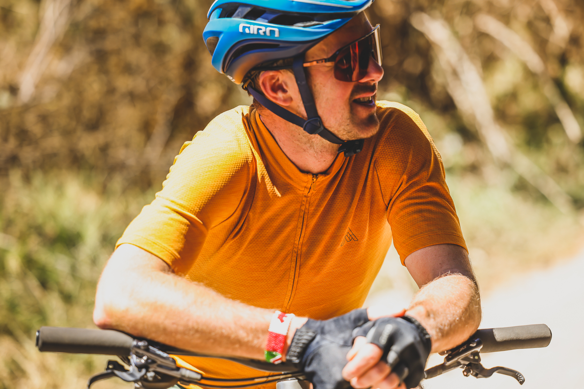 Close portrait of a rider in an orange jersey and blue helmet resting on the bars