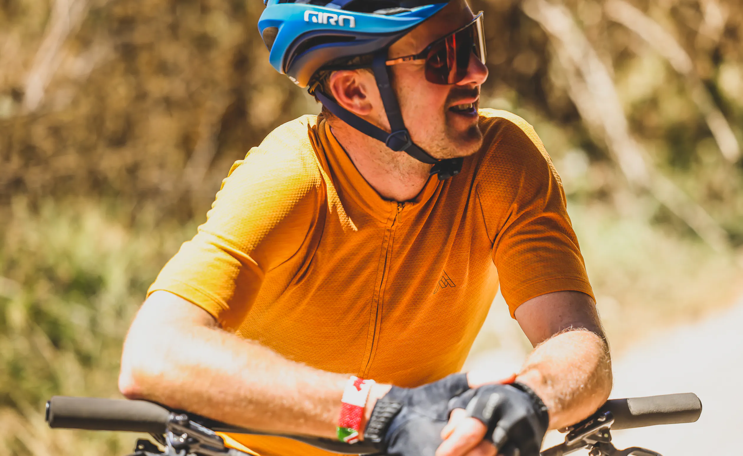 Close portrait of a rider in an orange jersey and blue helmet resting on the bars