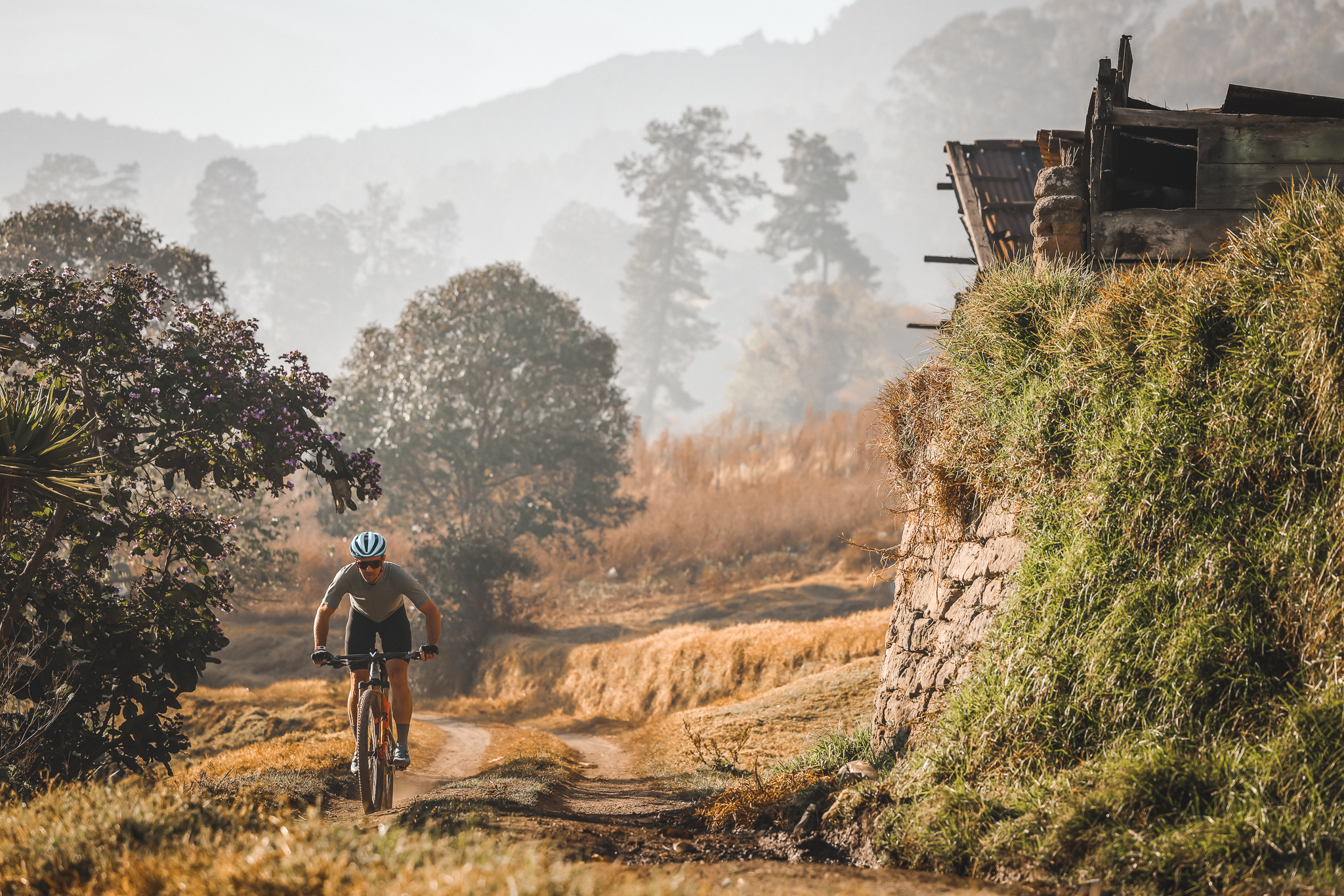 Rider climbing a dirt track past a stone bank in early morning haze