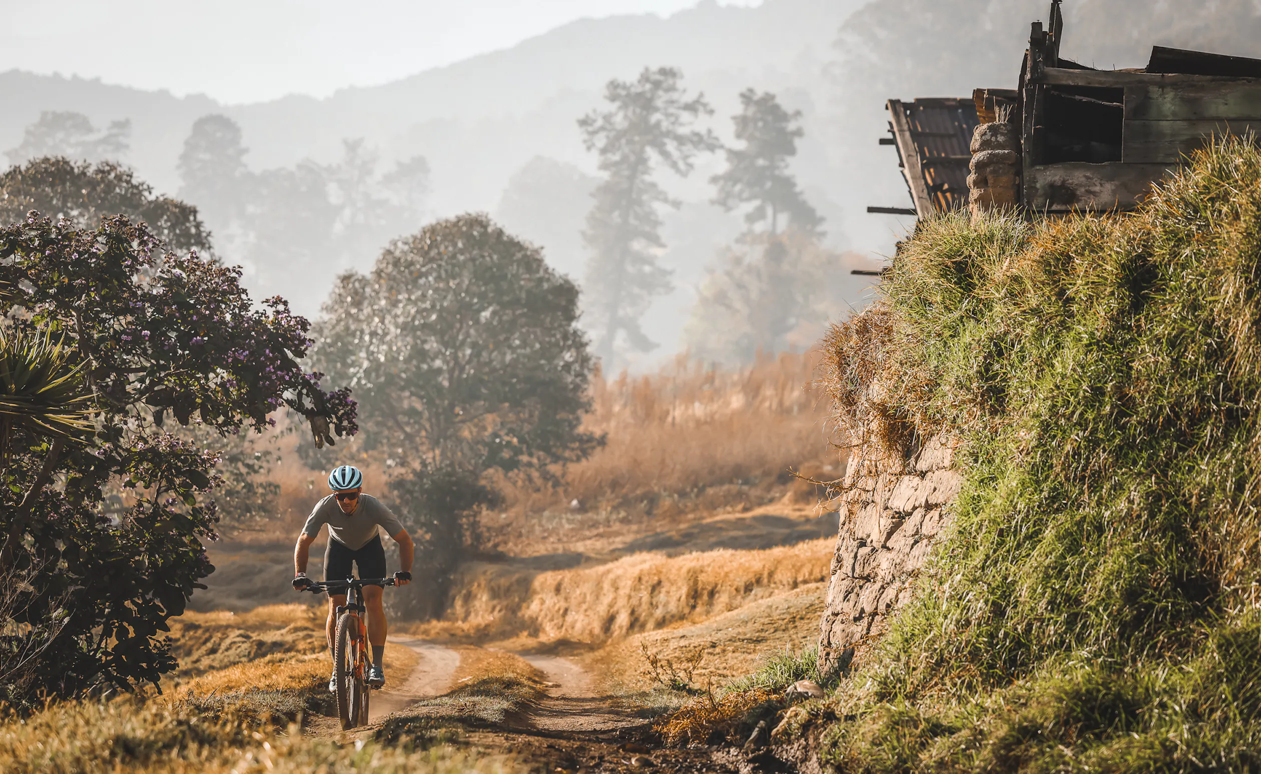 Rider climbing a dirt track past a stone bank in early morning haze