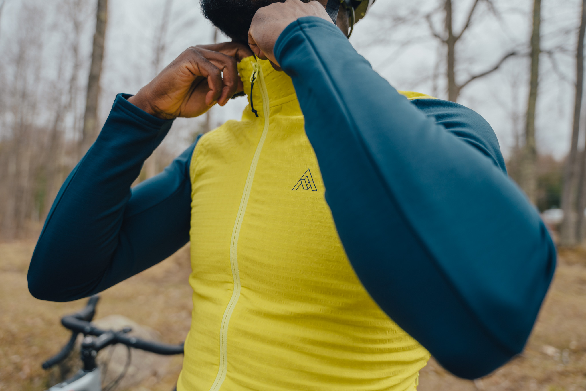 Rider zipping a yellow thermal jacket collar under a teal long-sleeve layer