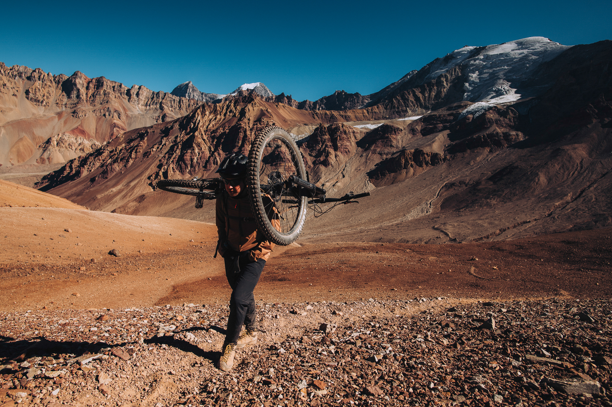 Rider carrying a bike on one shoulder across a red-brown desert basin