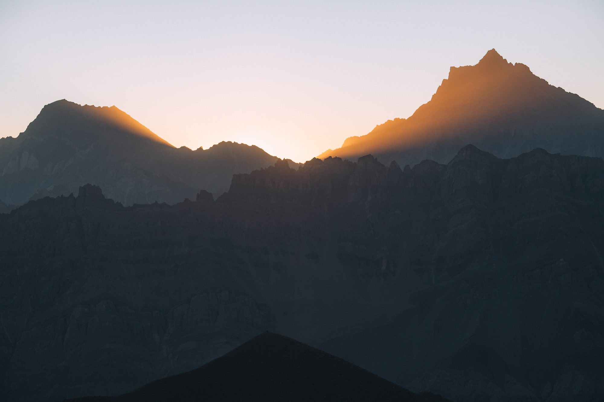 Sun rising behind a sharp ridgeline of dark Andean peaks