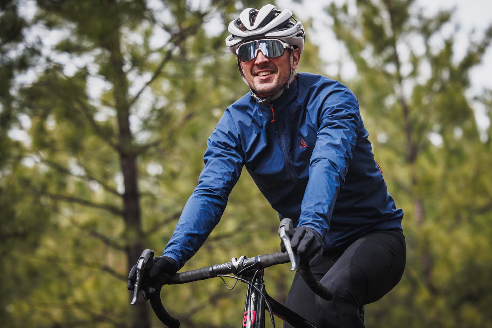 Road cyclist in a blue shell riding through open pine forest