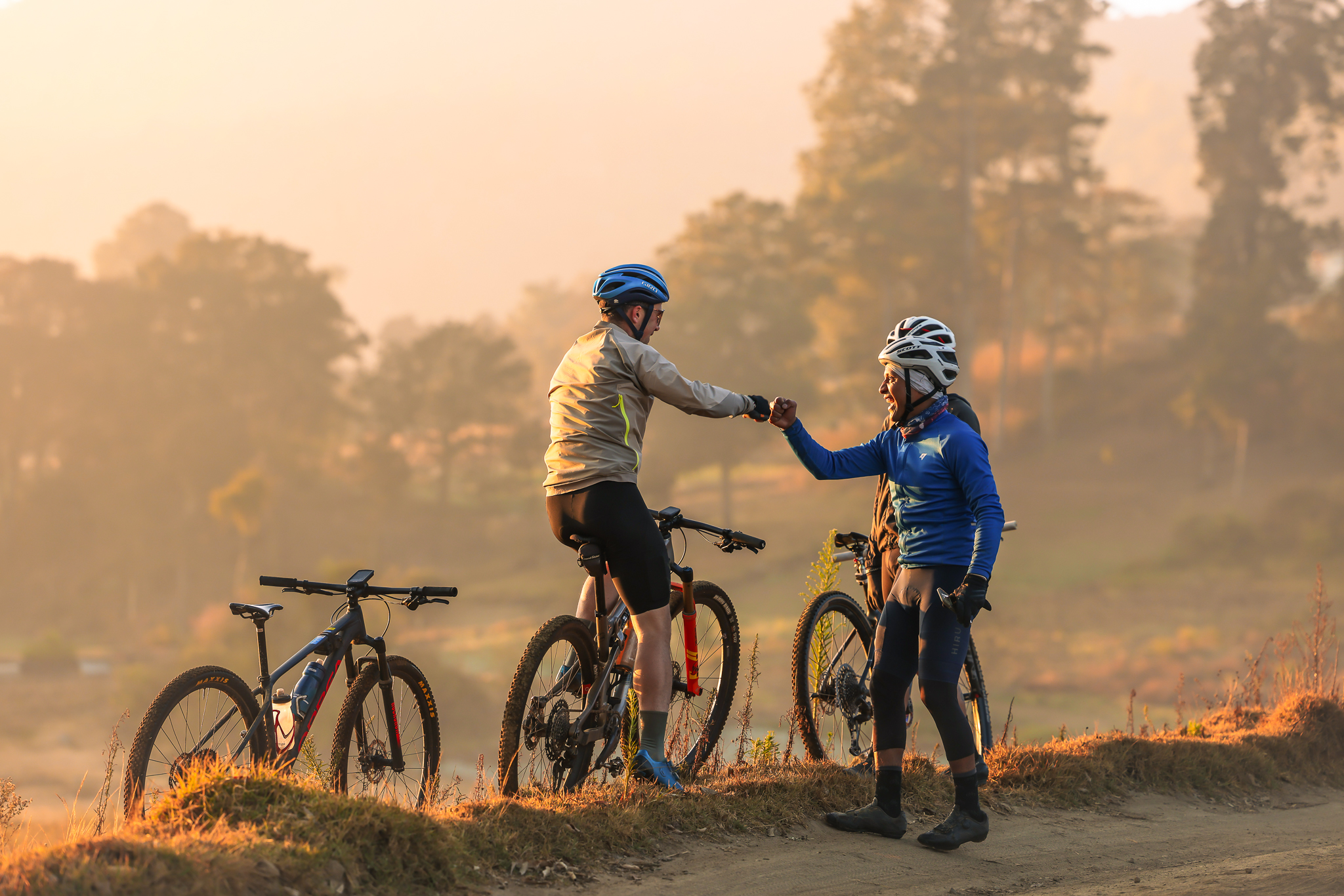 Two riders bumping fists on a dirt track at sunrise with bikes beside them