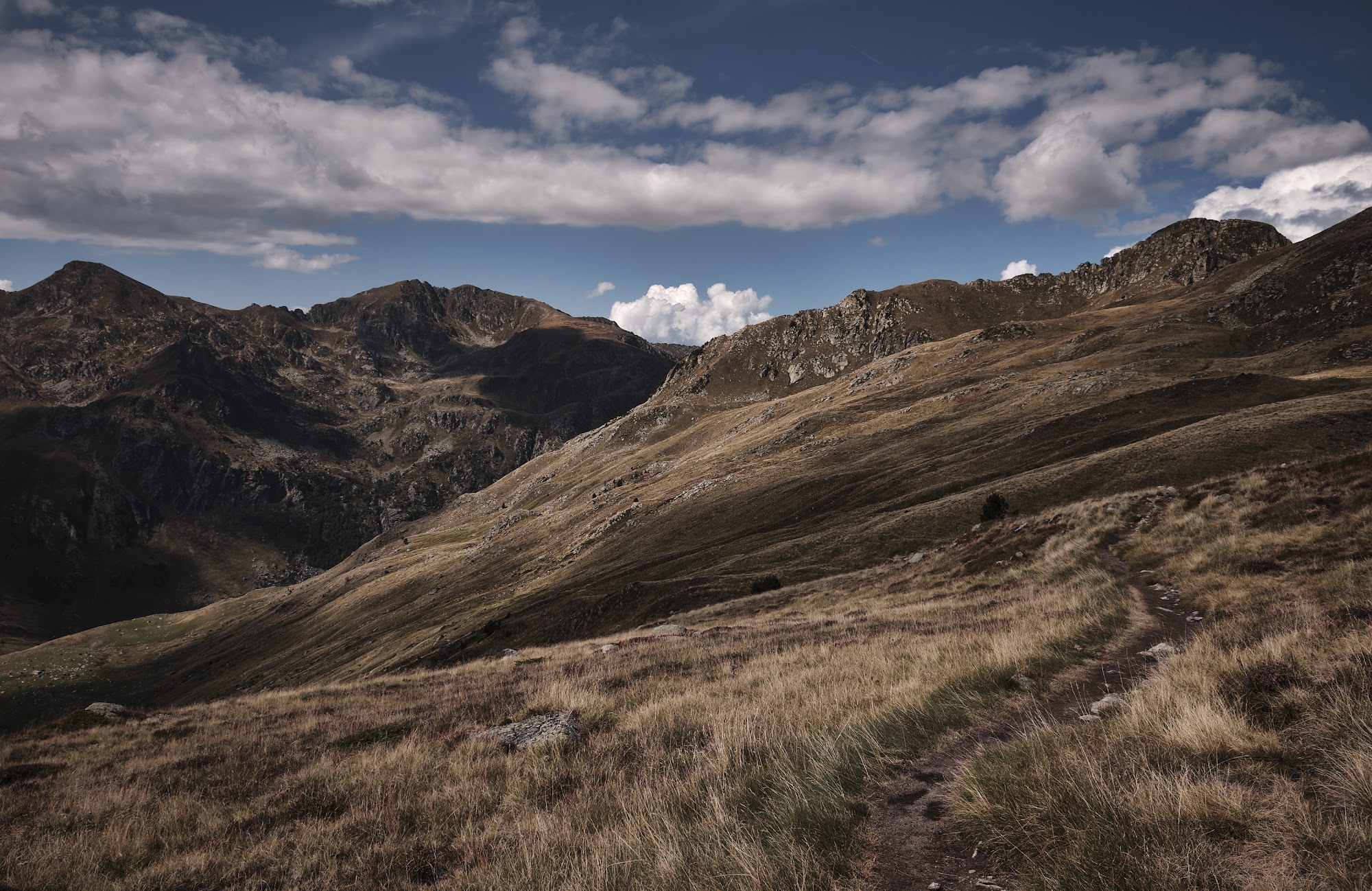 A footpath crosses an open grassy ridge with rocky summits and a deep valley beyond