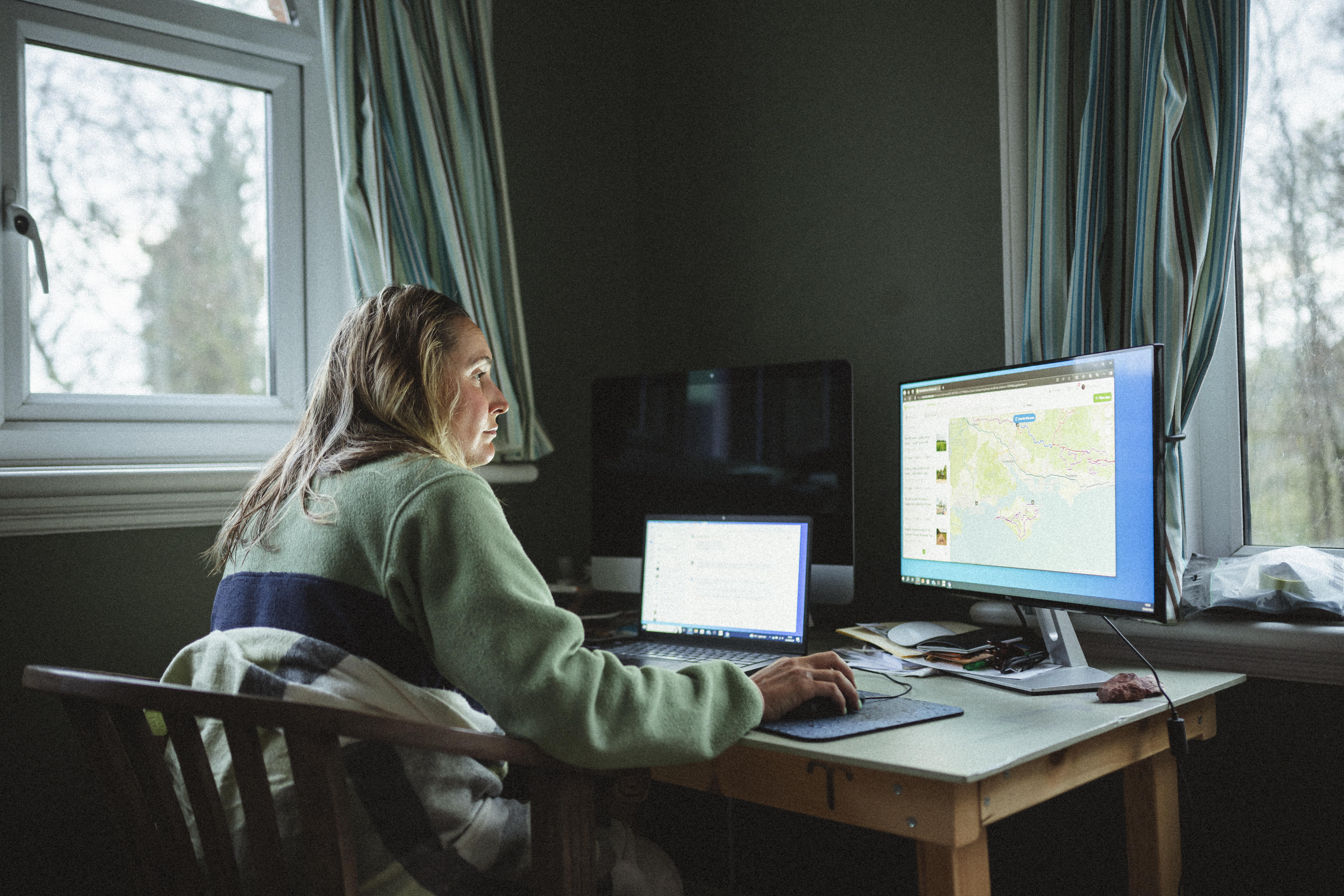 Rider back at a desk working at a laptop and monitor by a window