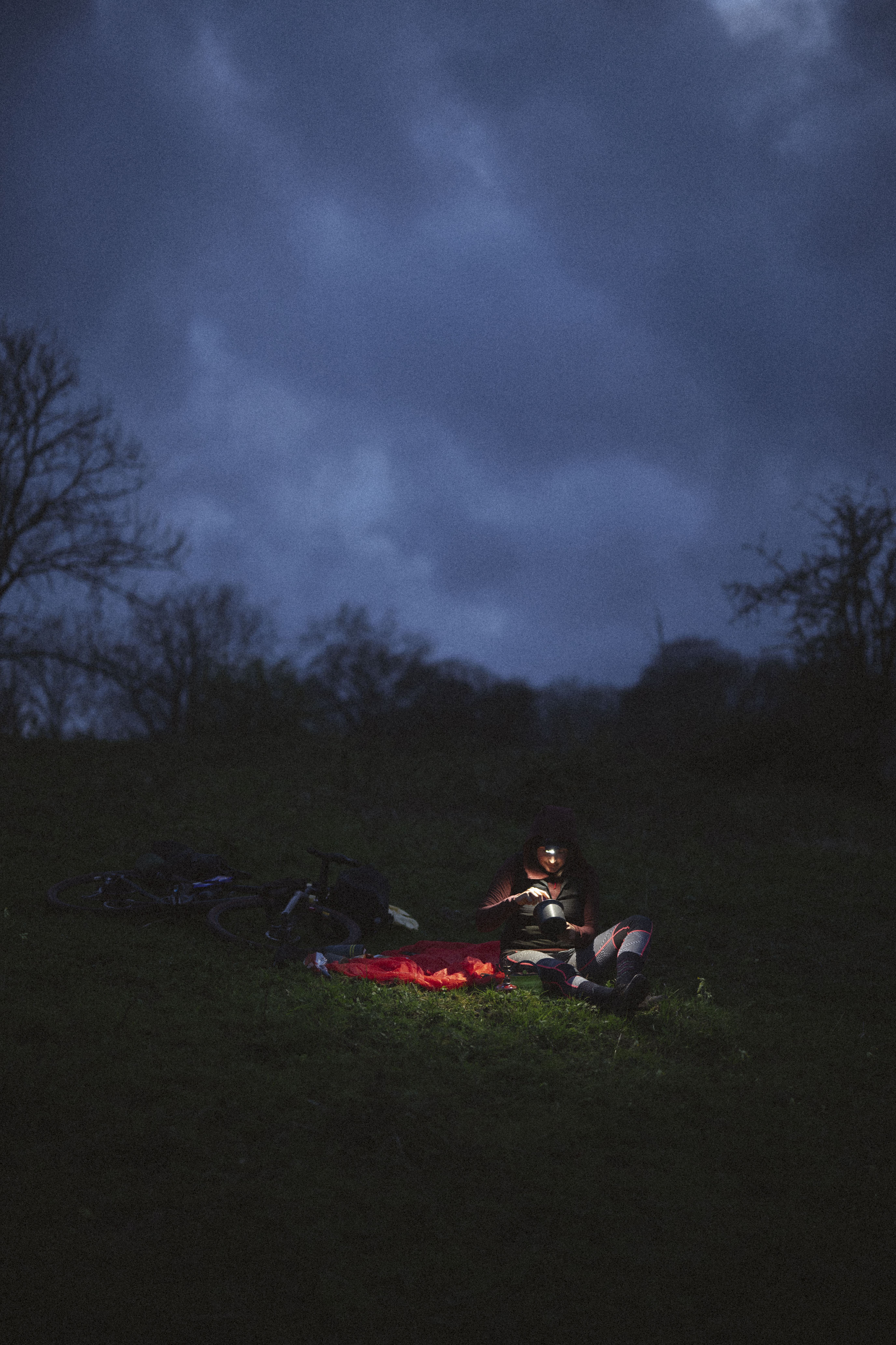 Camp at dusk with bikes laid down and a rider cooking by headtorch