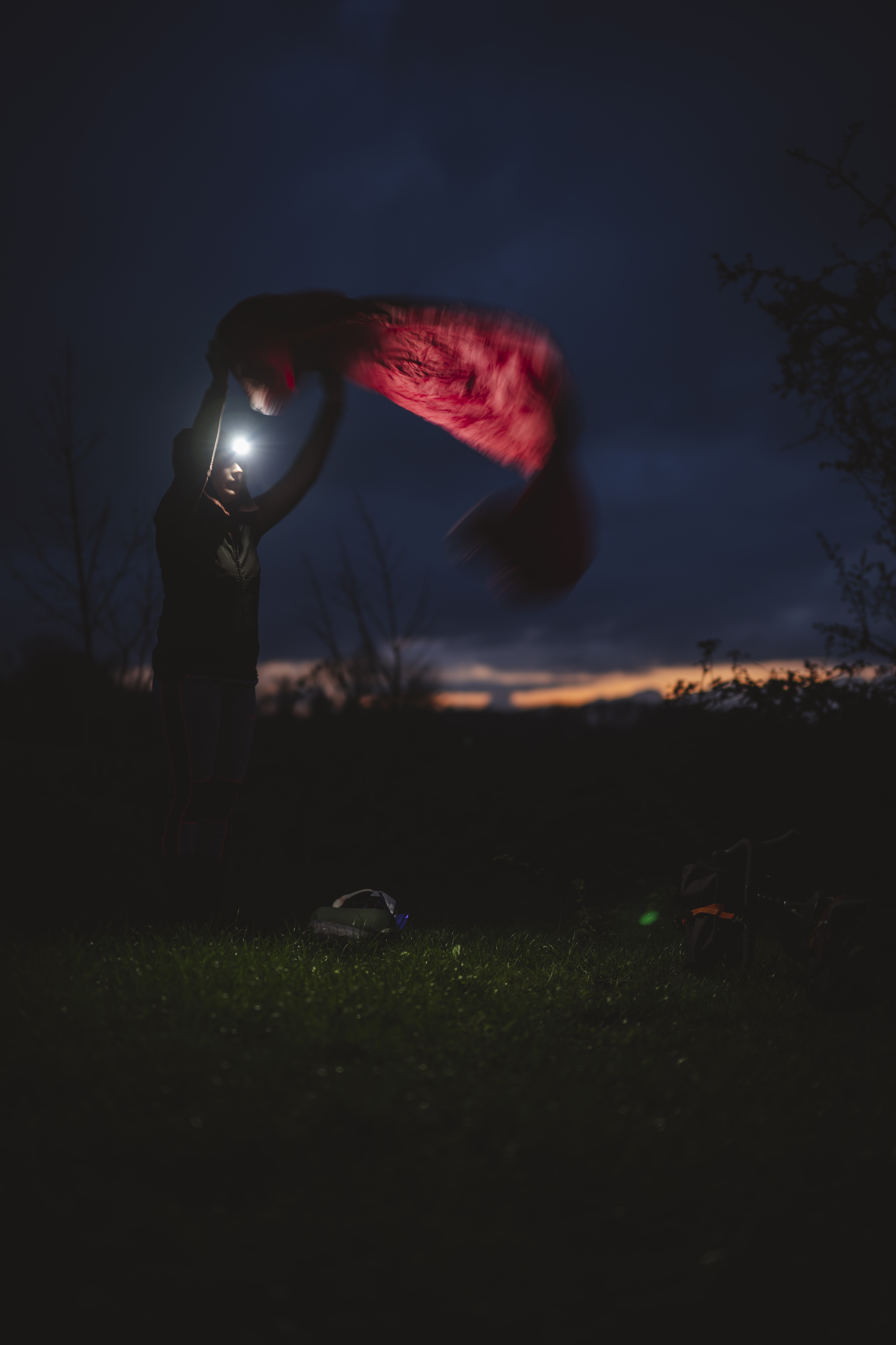 Rider shaking out a sleeping bag against a dark sunset sky