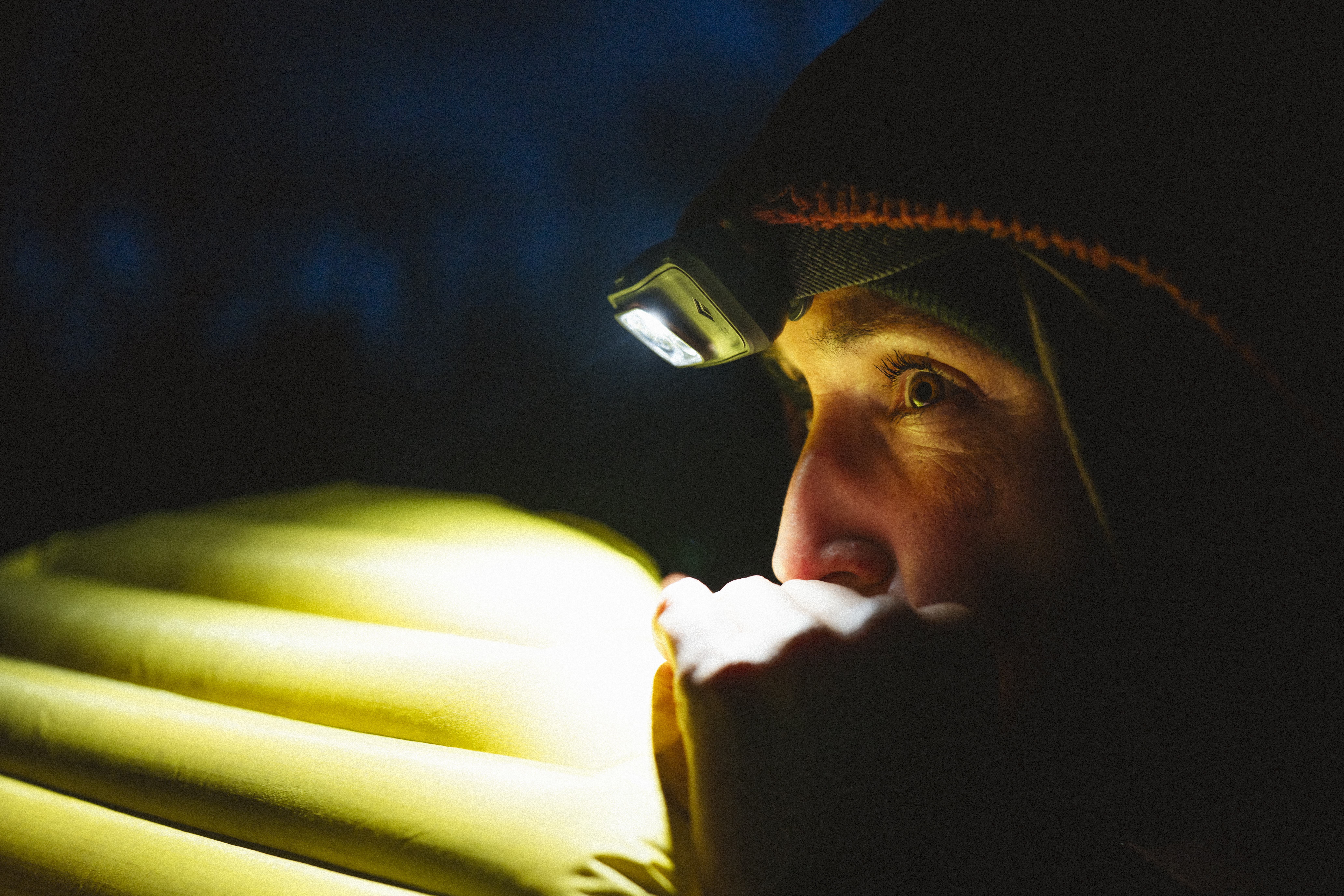 Rider in a headtorch inflating a sleeping mat at dusk