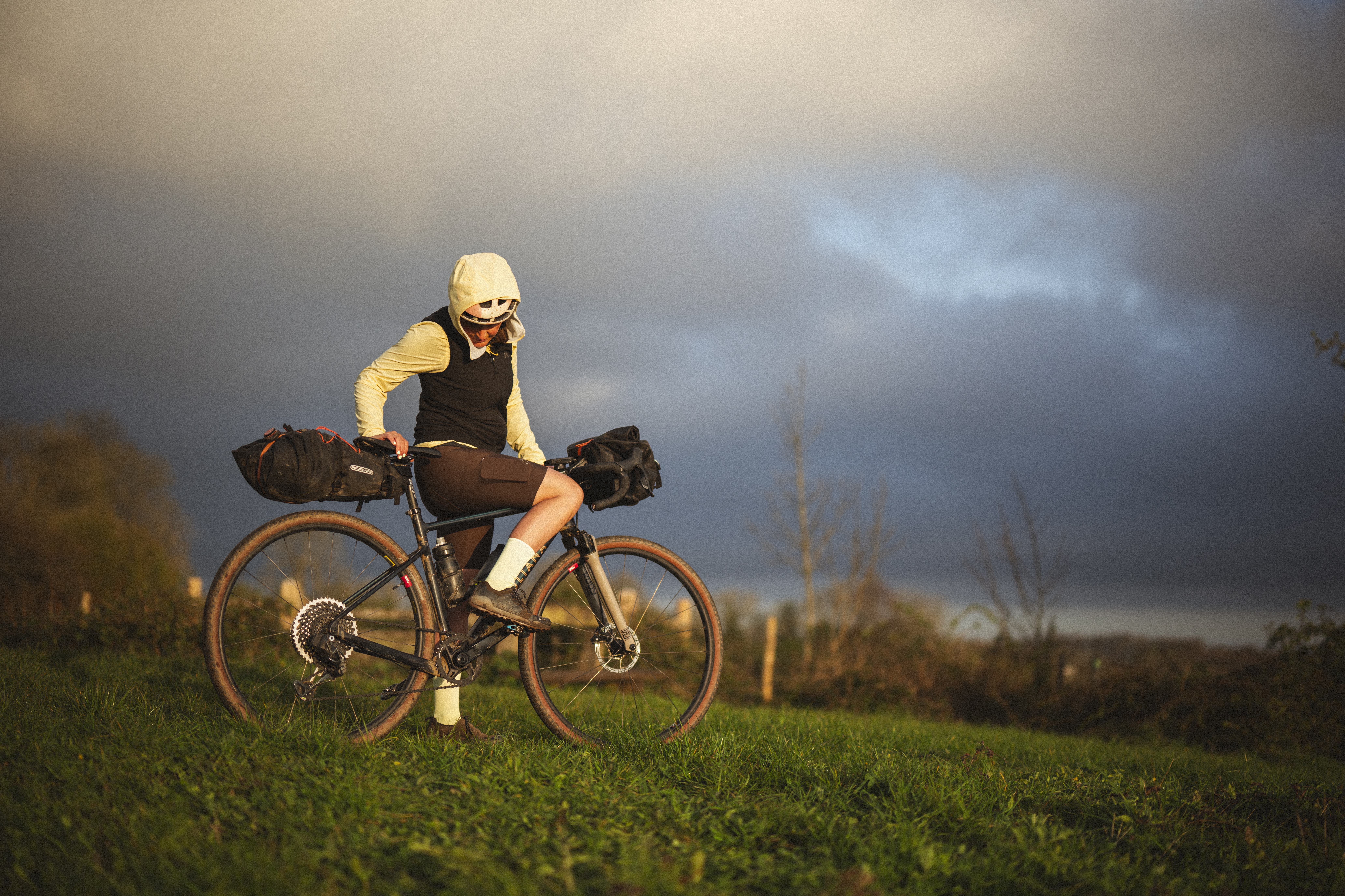 Rider on a loaded gravel bike on a grass ridge under a dark sky