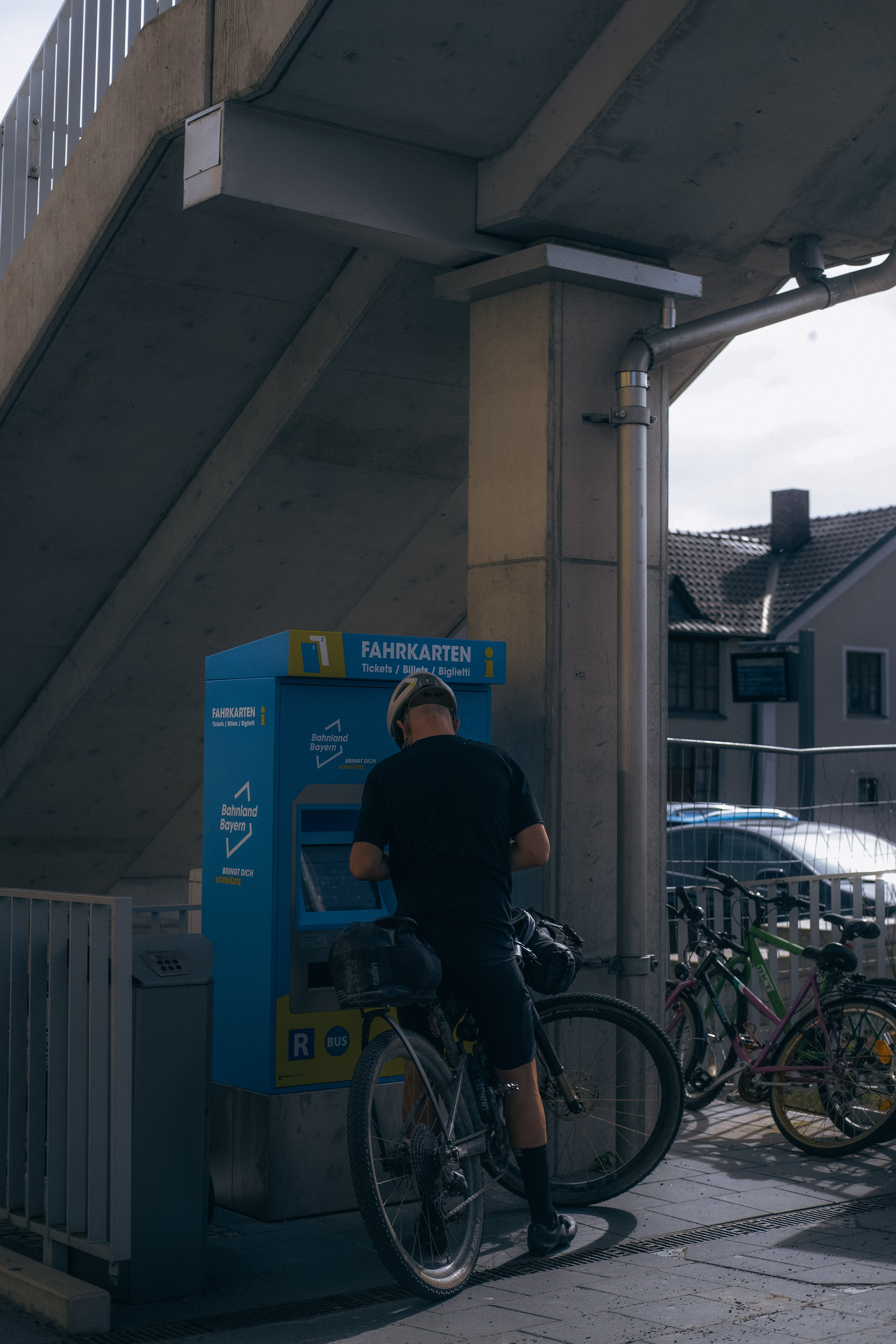 Cyclist at a blue Bahnland Bayern ticket machine with a loaded bike beside them