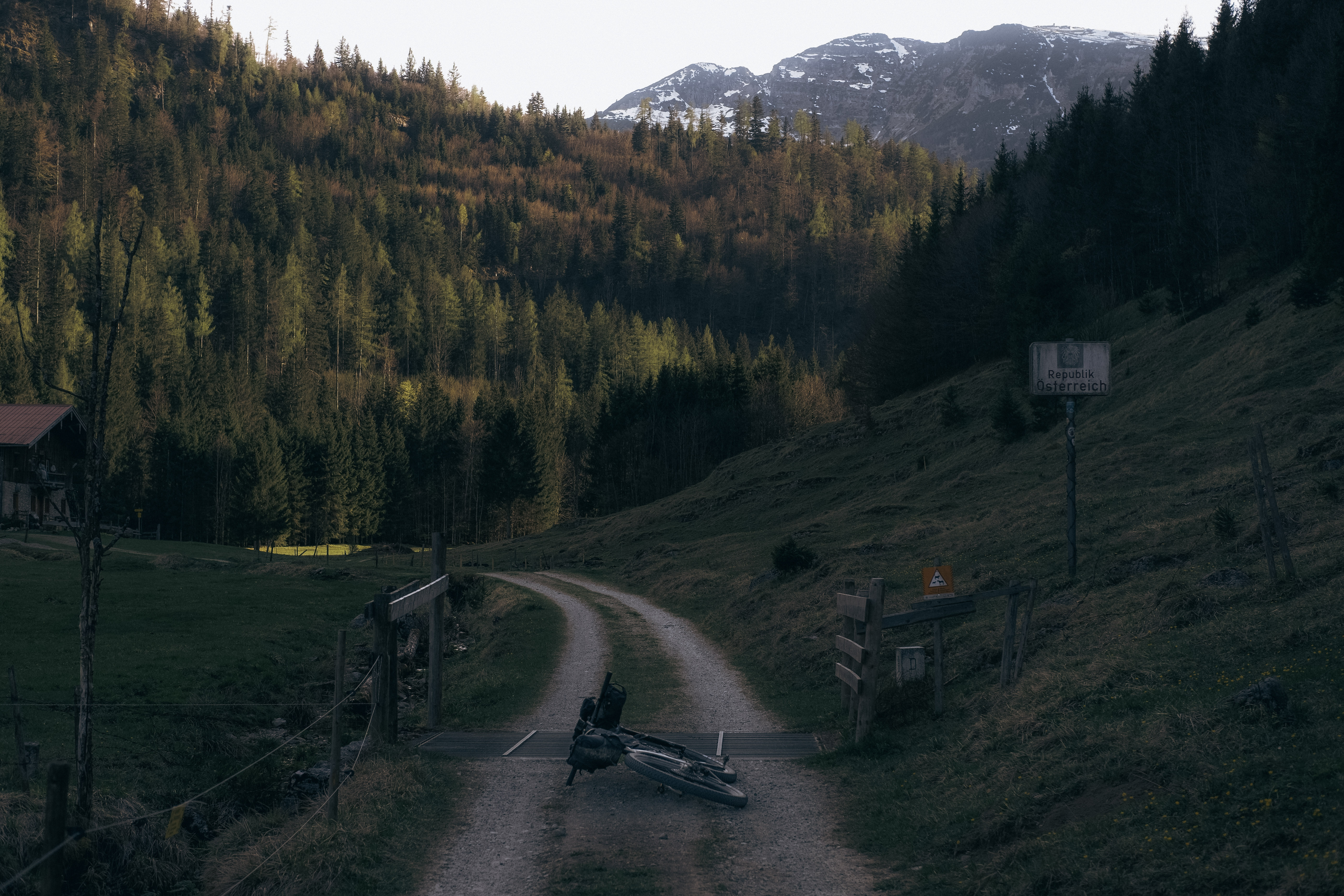 Loaded bikepacking bike lying on a gravel road beside a Republik Österreich border sign
