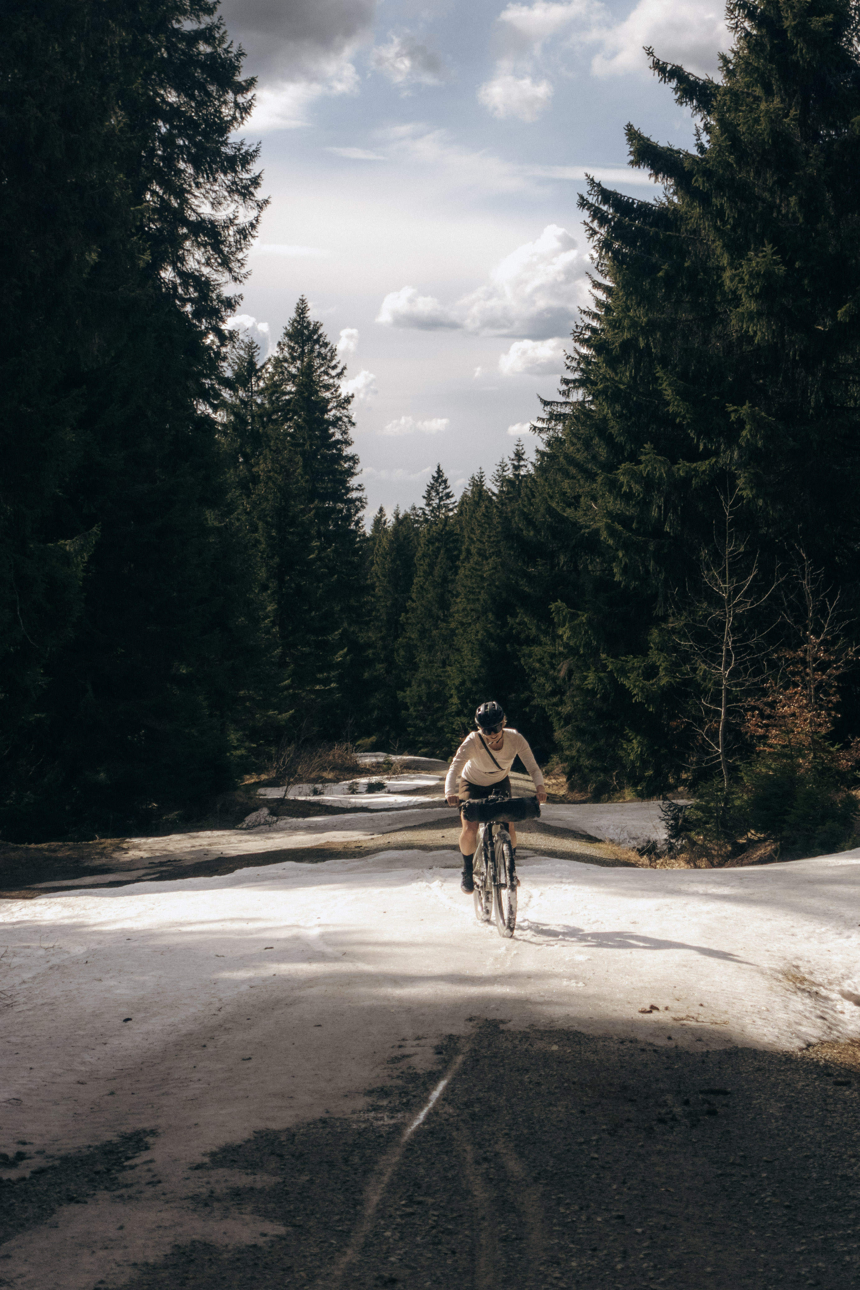 Rider climbing a snow-covered forest road in low afternoon sun