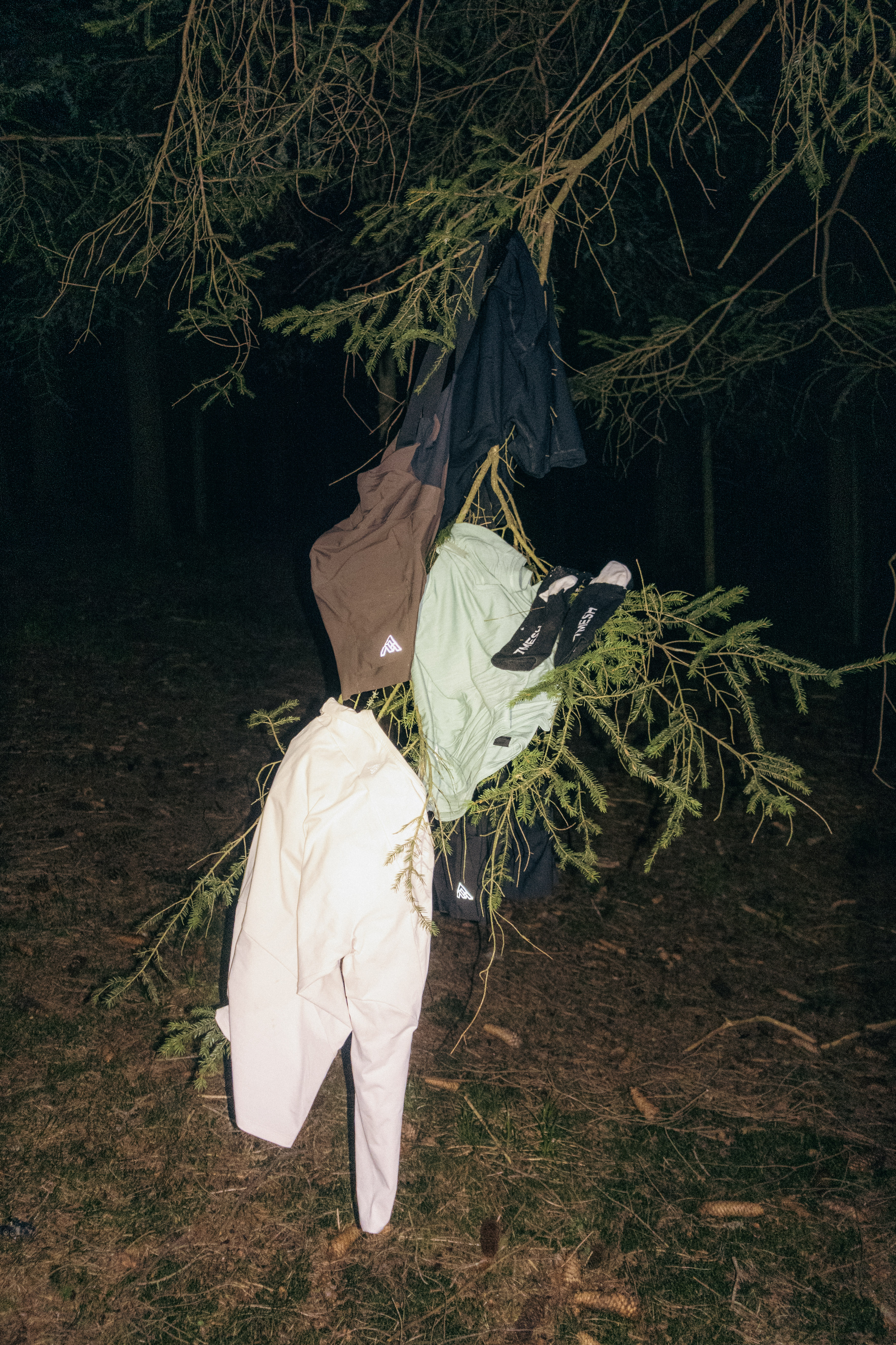 Cycling clothing and socks hung to dry on a spruce branch at night