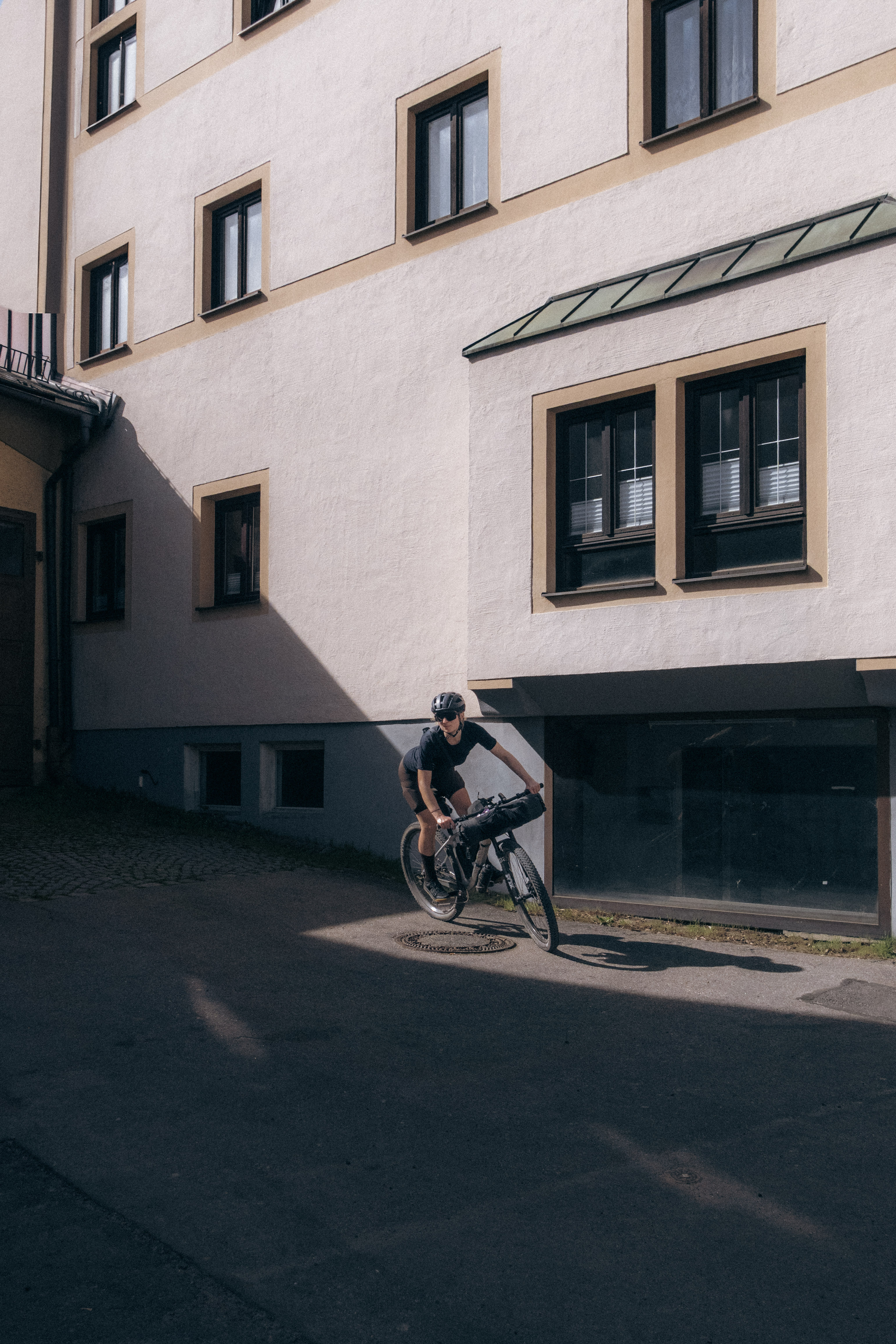 Rider on a loaded bike rolling past a pale rendered building on a cobbled village street