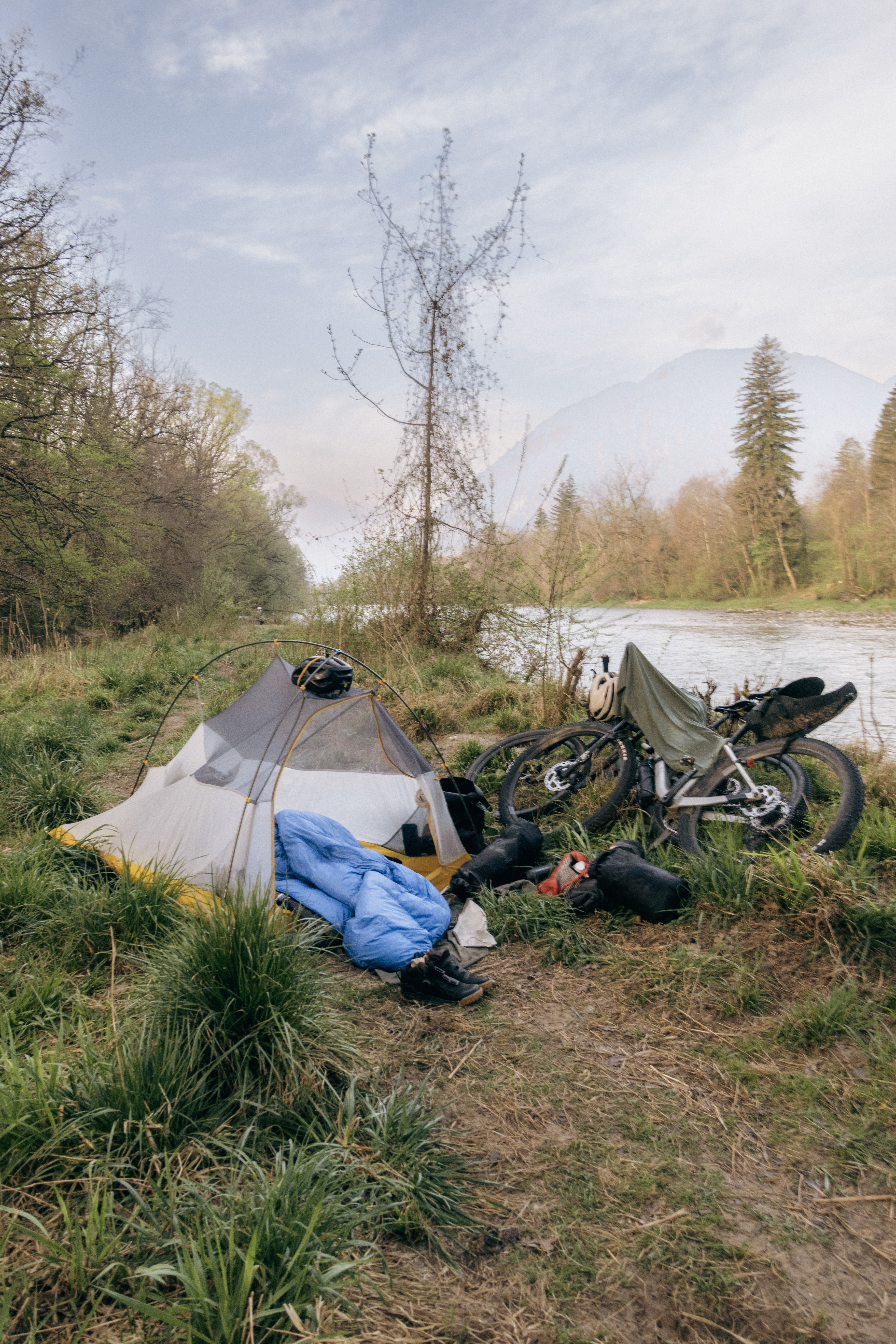 Tent, sleeping bag and 2 loaded bikes pitched on a grassy riverbank