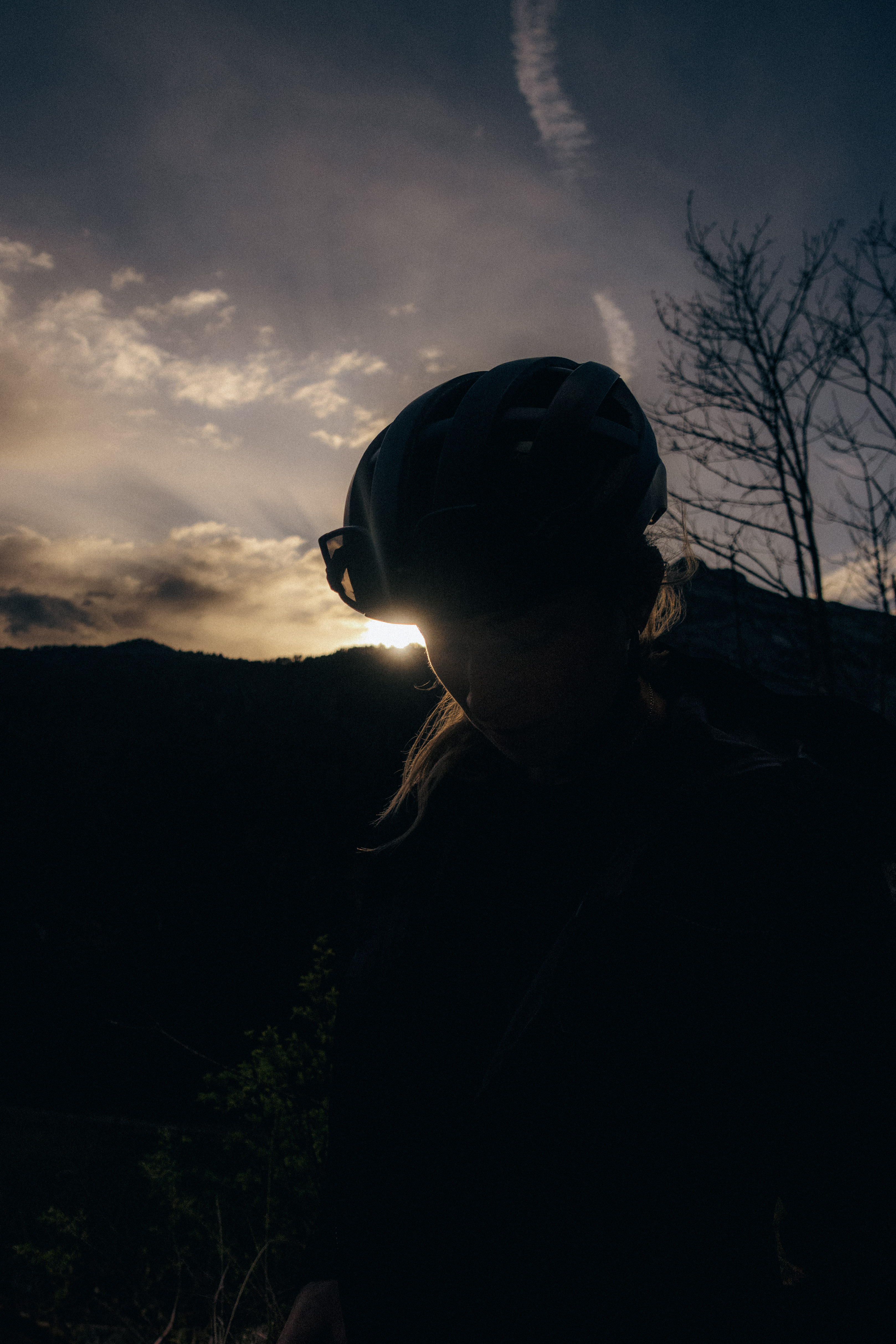 Rider in a helmet silhouetted against the sun sitting low over a wooded ridge