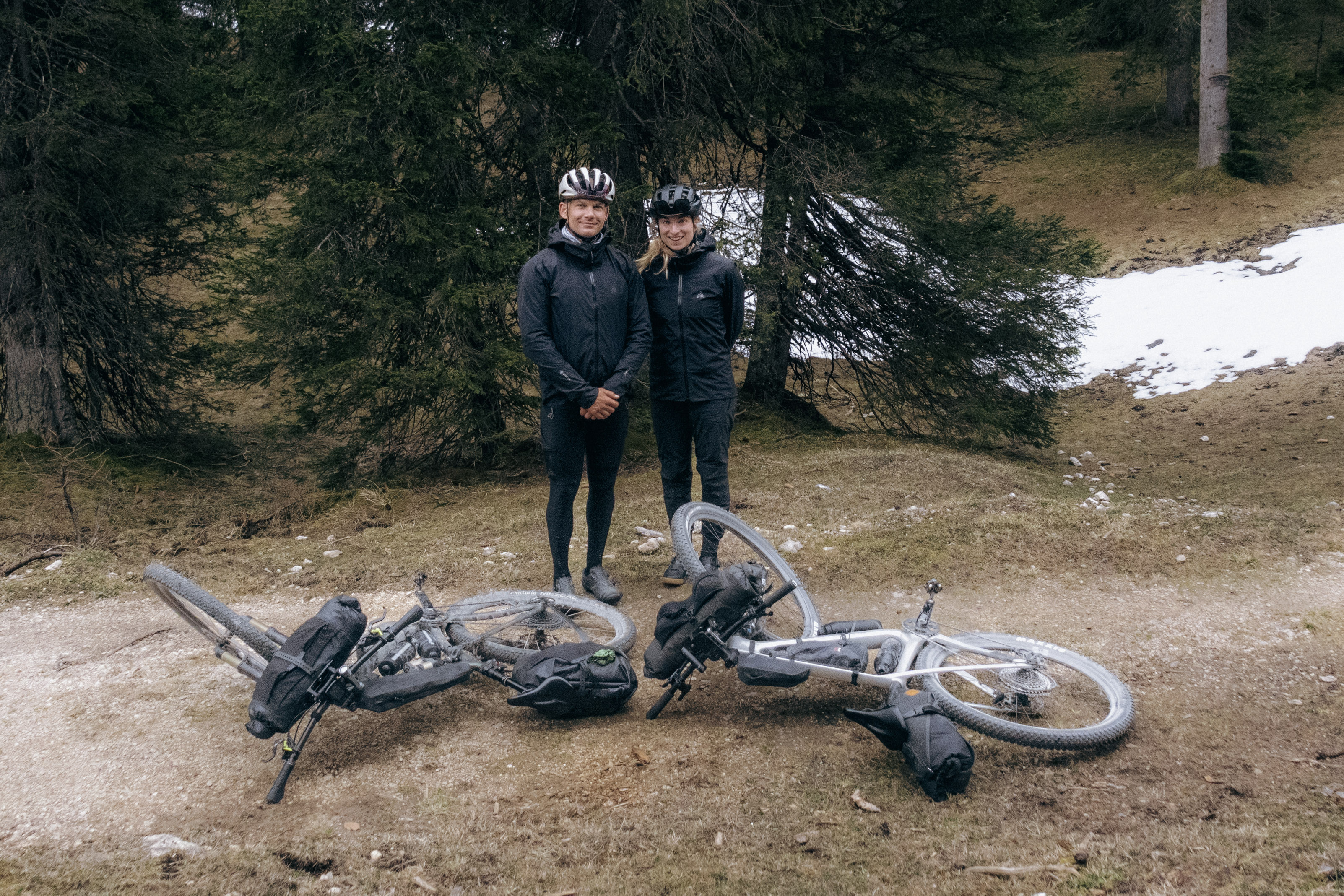 Alex Kopp and Karen Ekman standing behind two loaded bikepacking bikes at a snowy forest edge