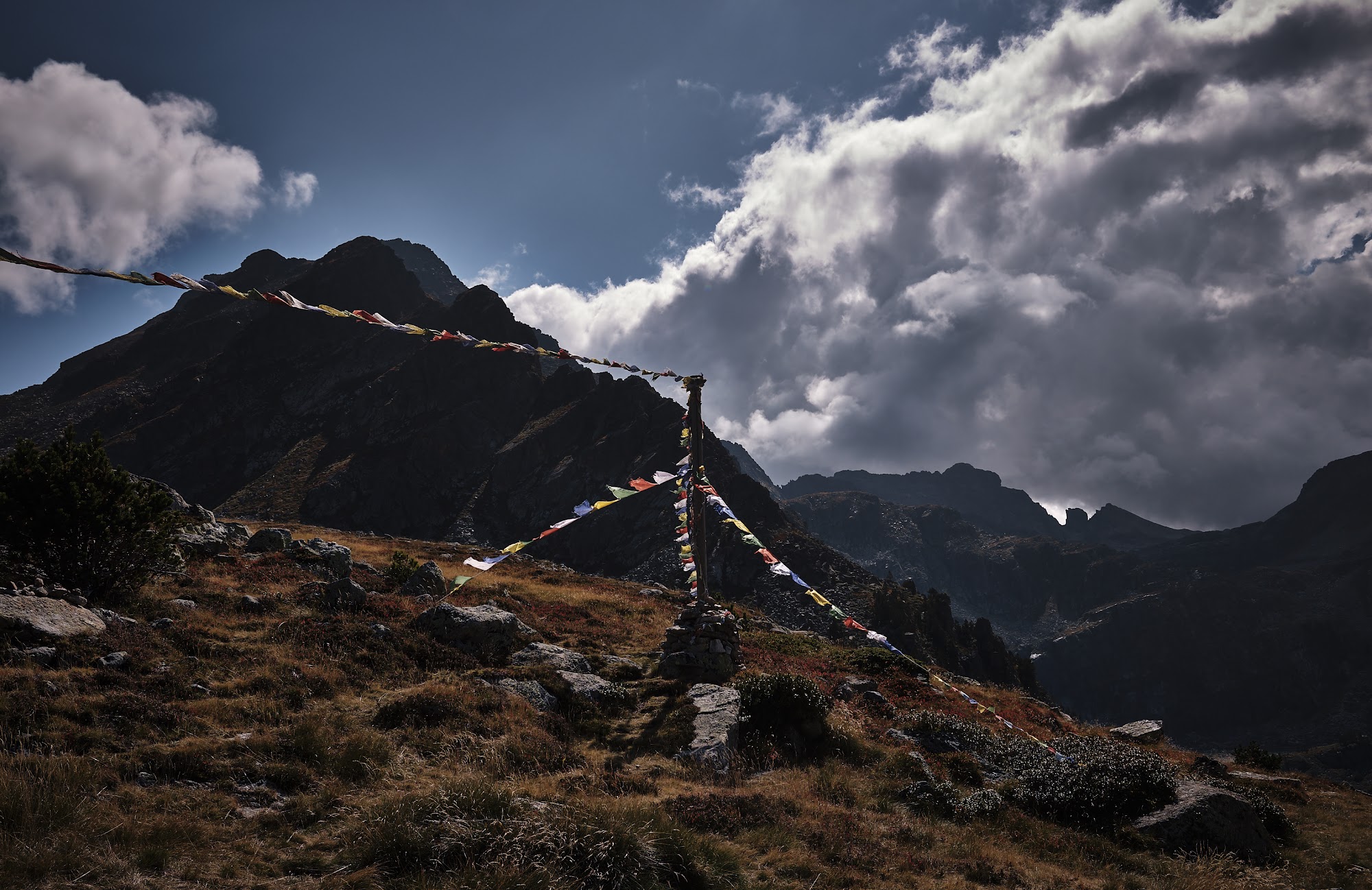 Prayer flags strung from a pole on a rocky cairn, dark mountains behind