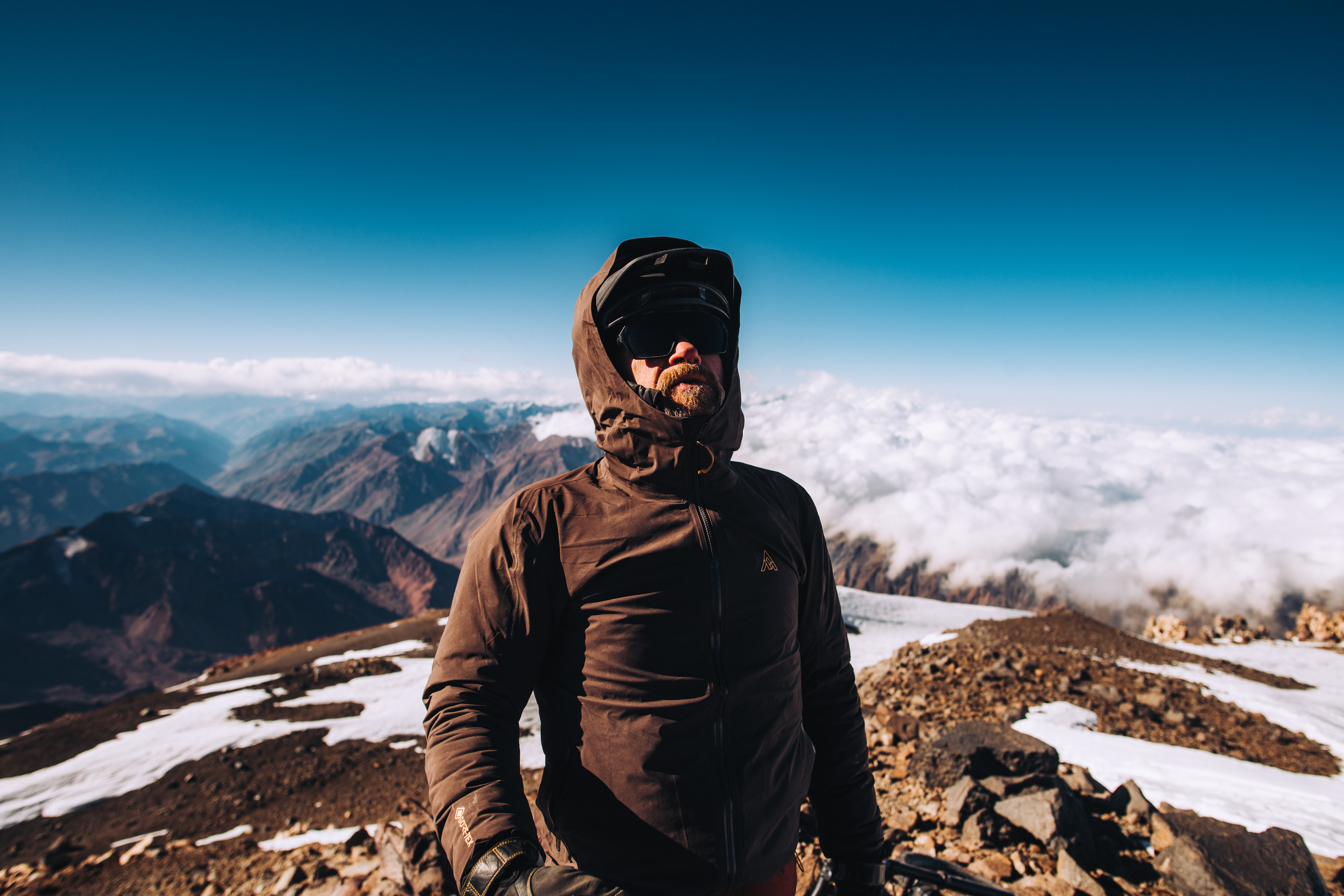 Rider in a hooded jacket on a summit above a sea of cloud
