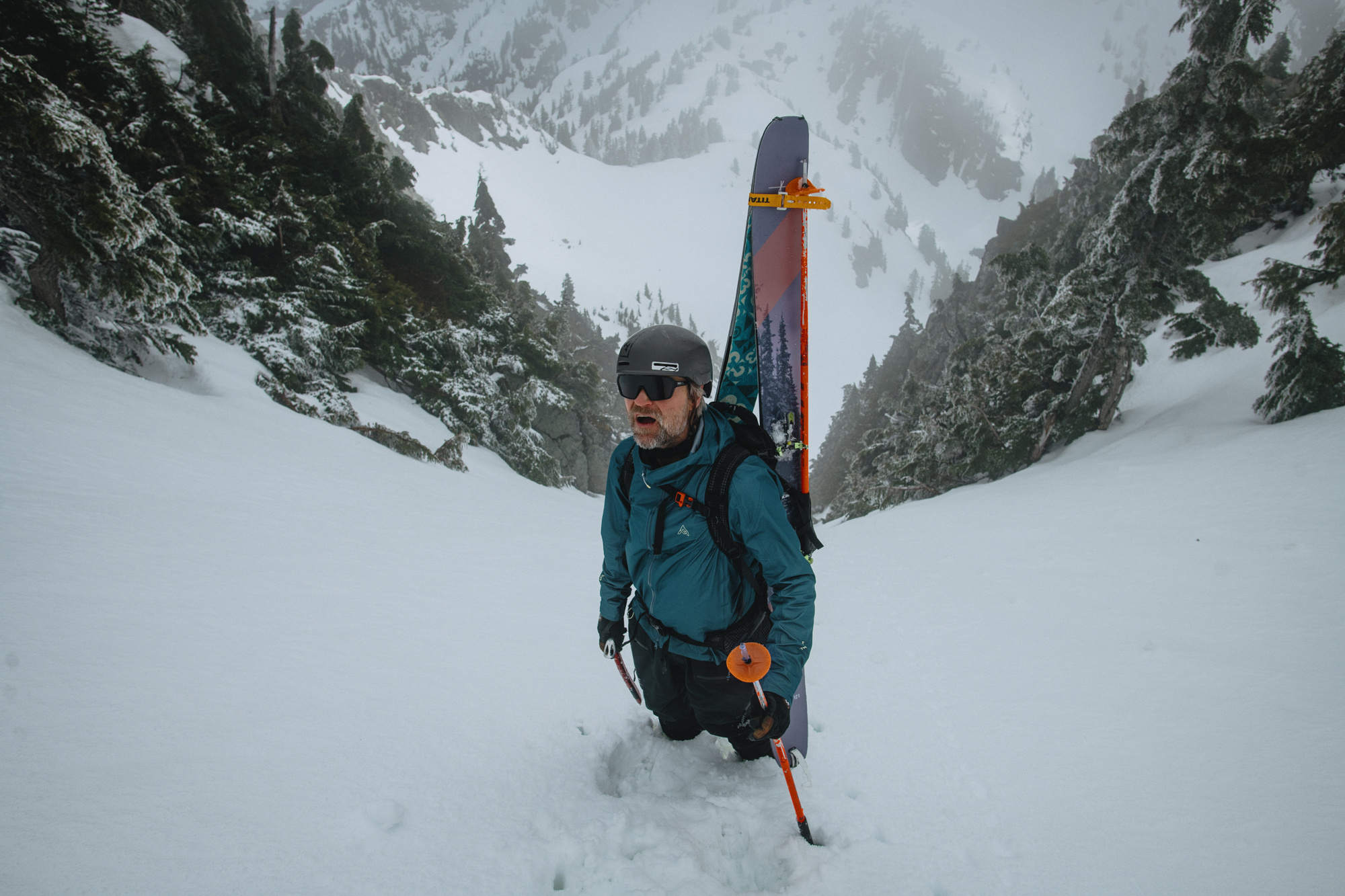 Skier with skis on their pack breaking trail up a snowy couloir