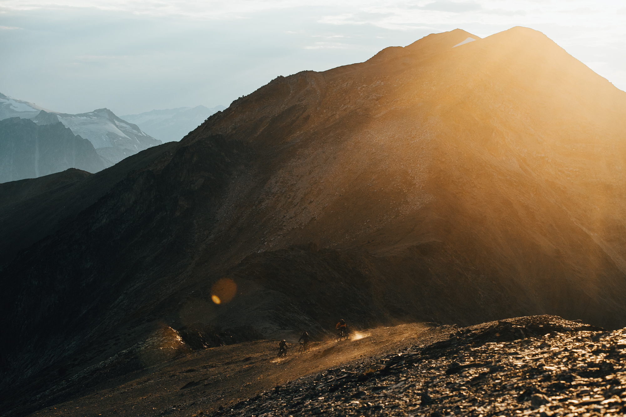 Distant riders on a sunlit ridge with sun flaring over the crest