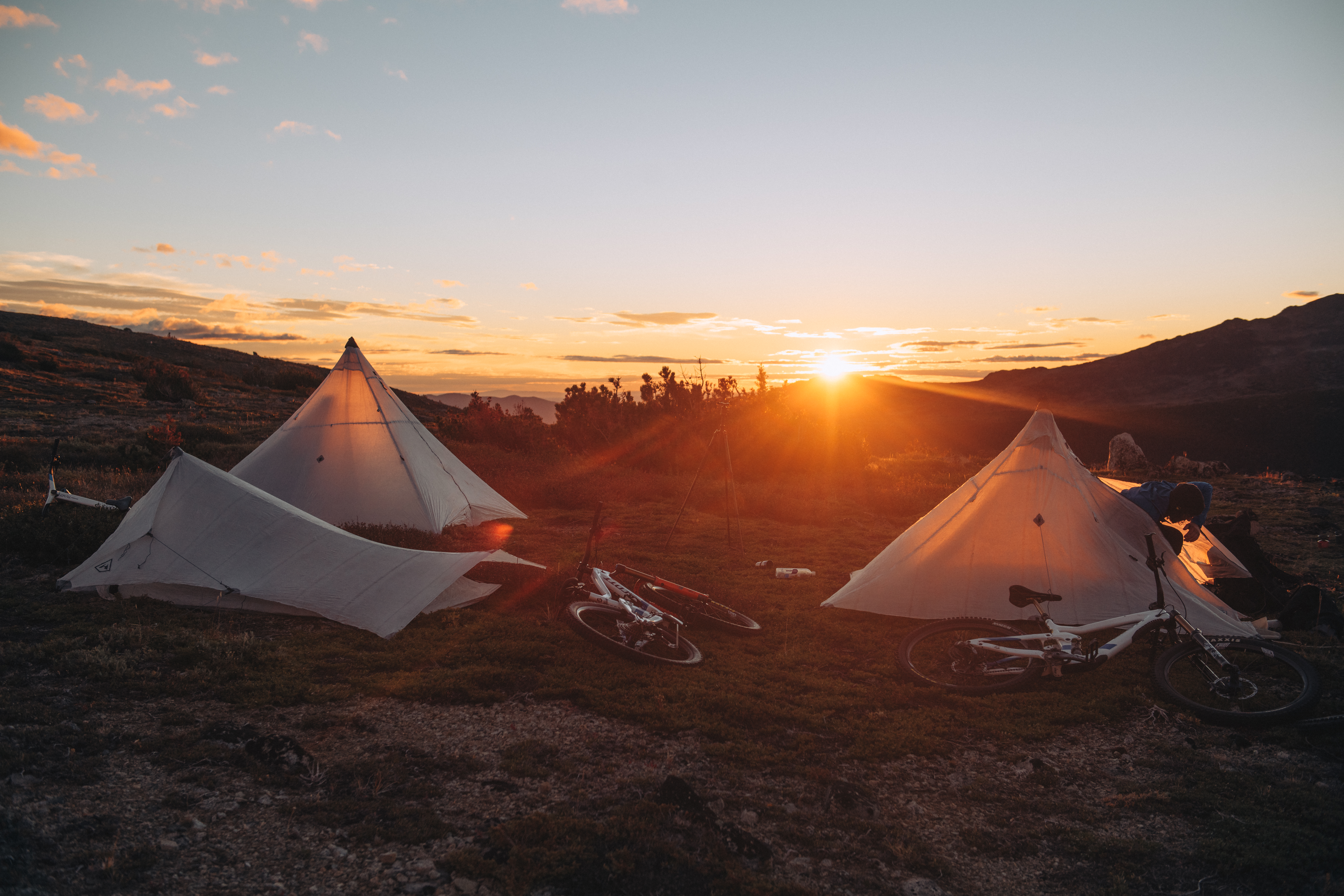 Two pyramid tents and bikes at camp with the sun on the horizon