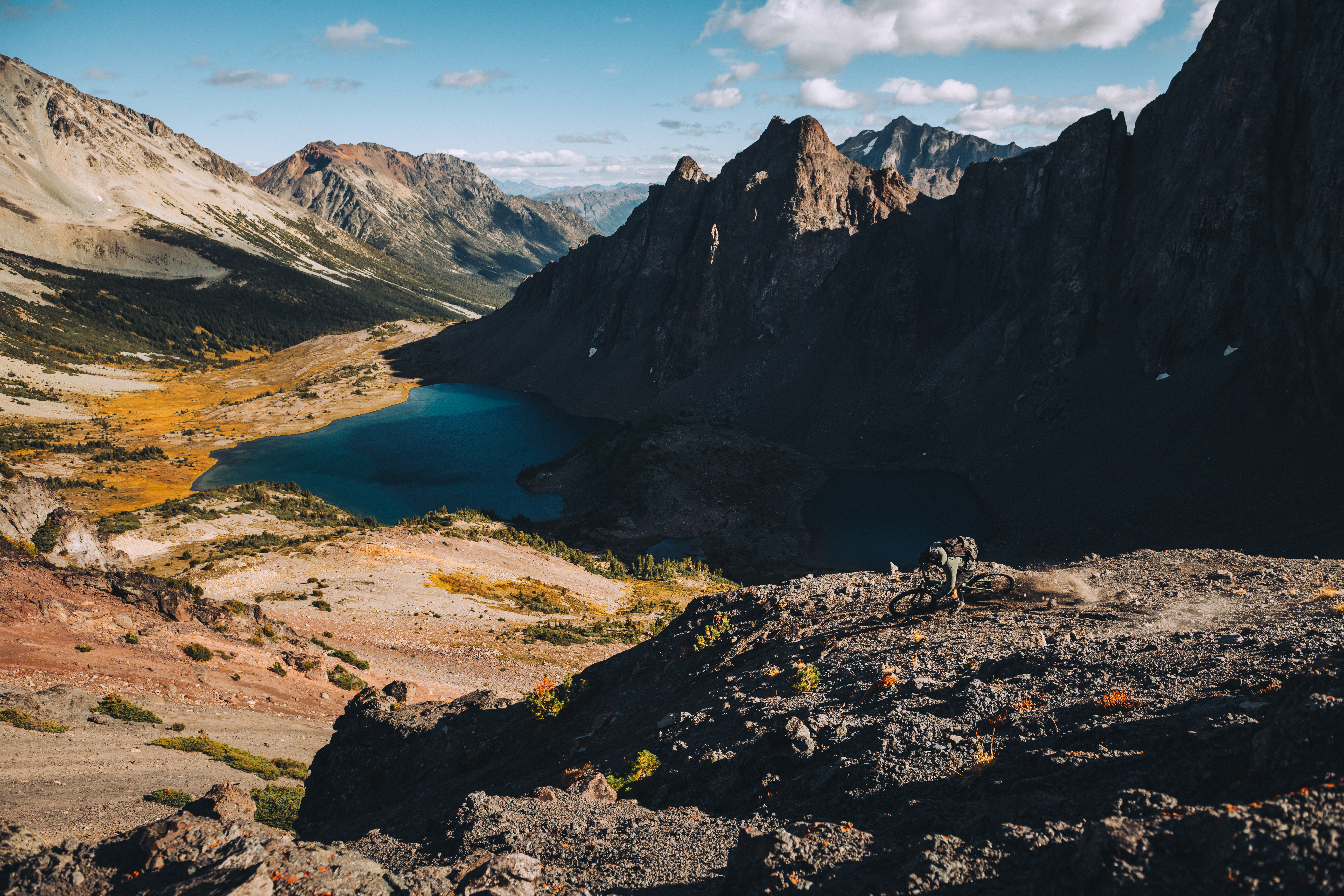 Rider on a dark rock rib high above a turquoise alpine lake