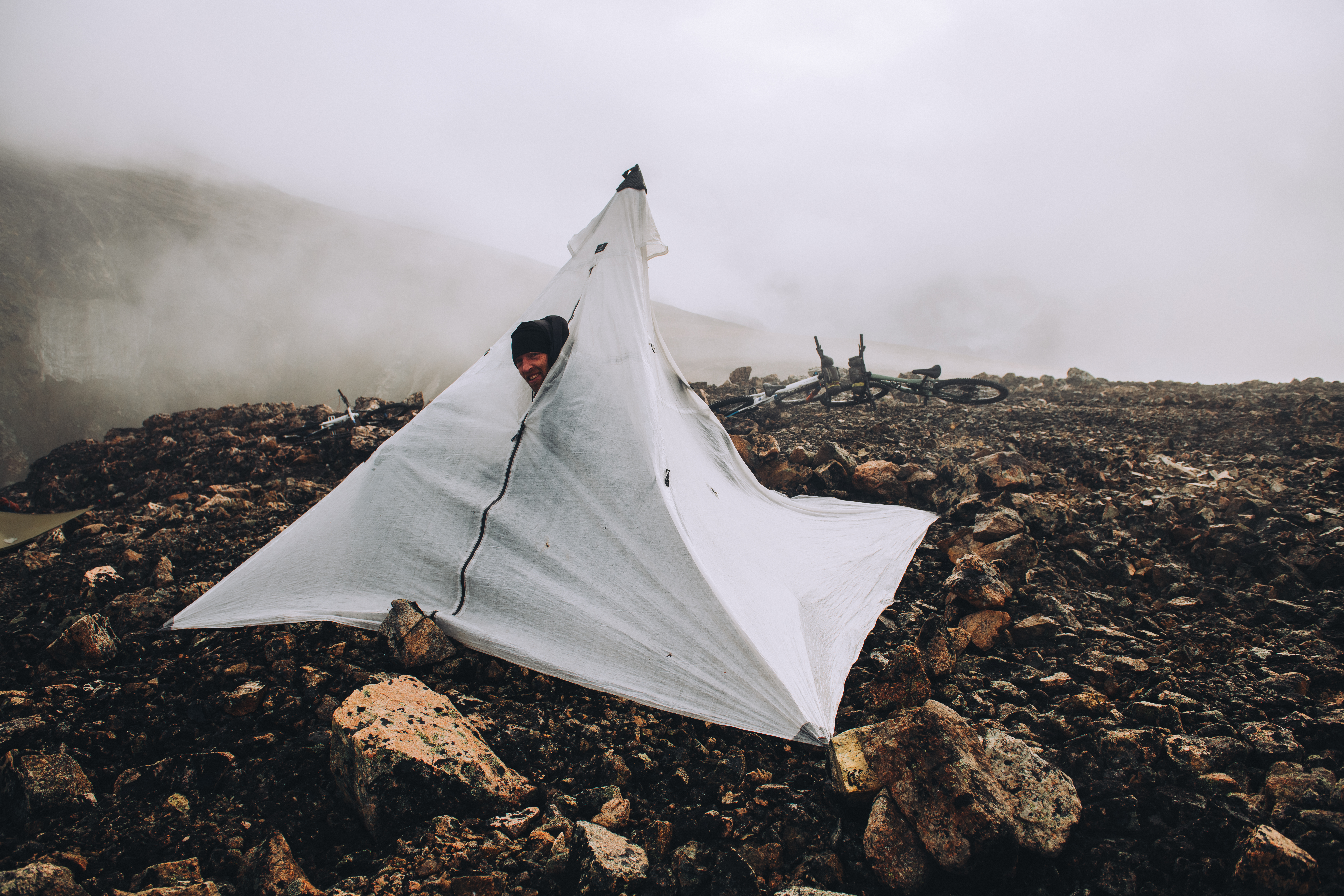 Rider sheltering in a white pyramid tarp pitched on rock in cloud