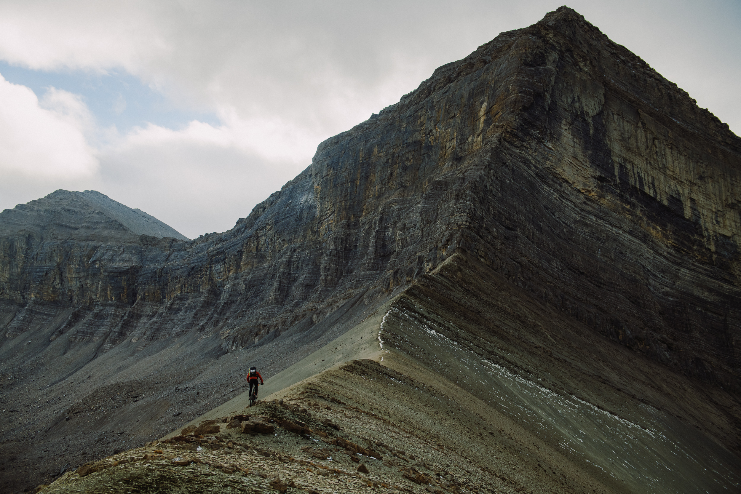 Lone rider pushing up a narrow ridge below a large striated peak