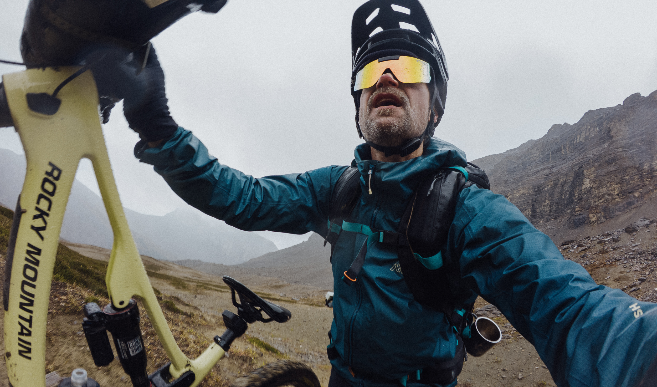 Rider in a blue shell holding up a yellow mountain bike, out of breath